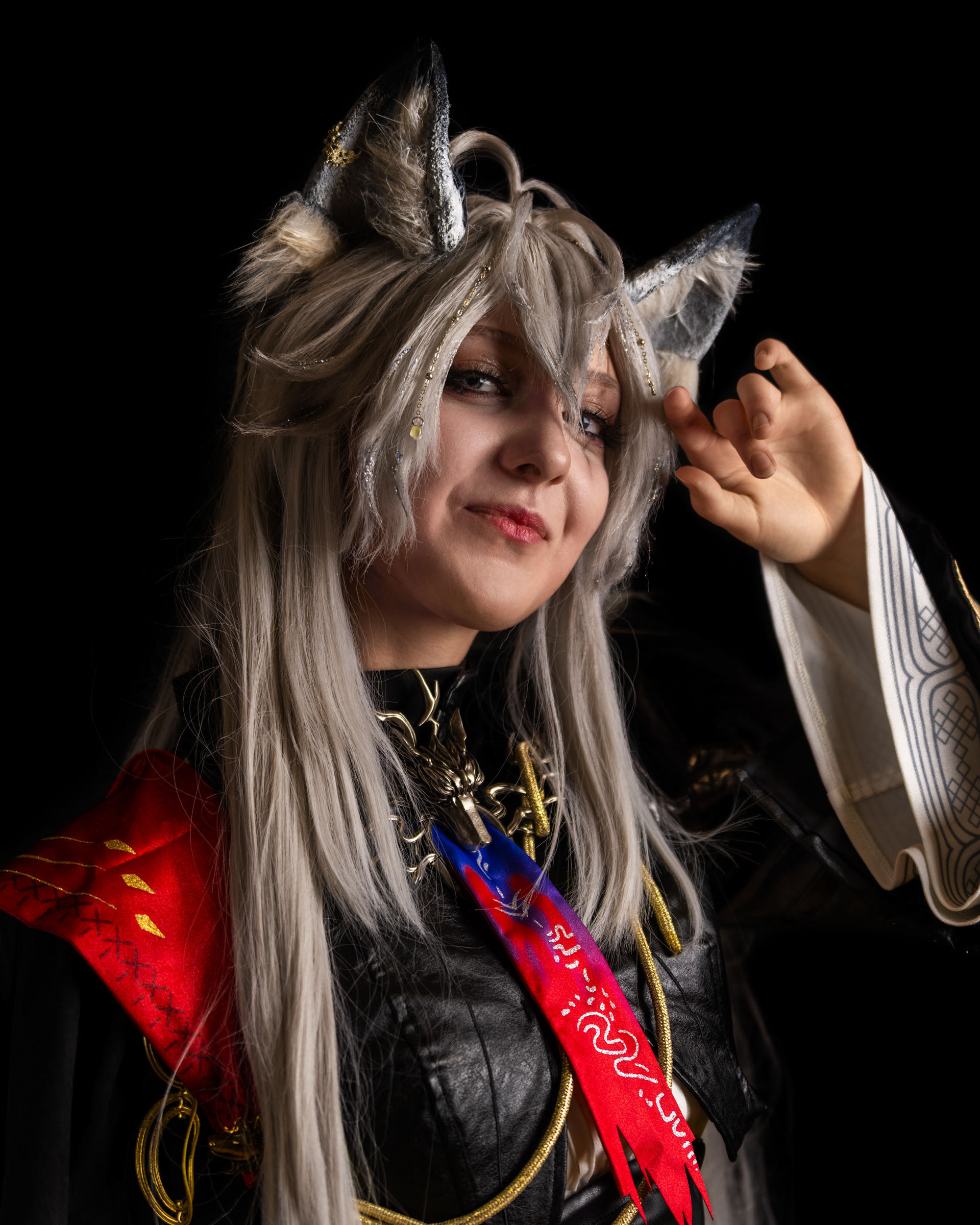 Close-up of cosplayer nether_cos as Lappland from Arknights, showing silver wolf ears, long silver hair and expressive facial features in a dark studio setting.