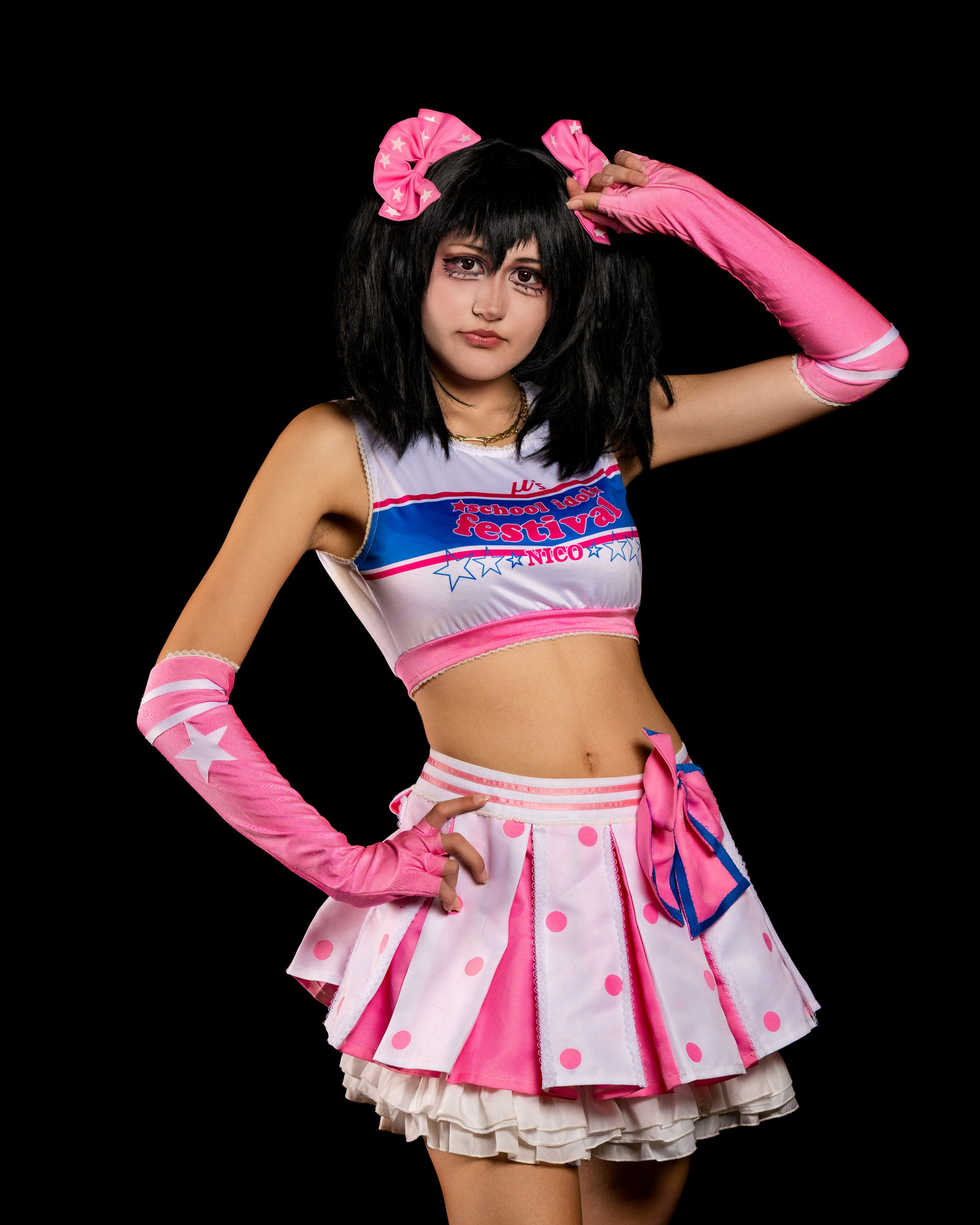 Studio shot of may_c0z as Nico Yazawa posing with one hand near her face, showing the bright pink gloves and layered skirt.