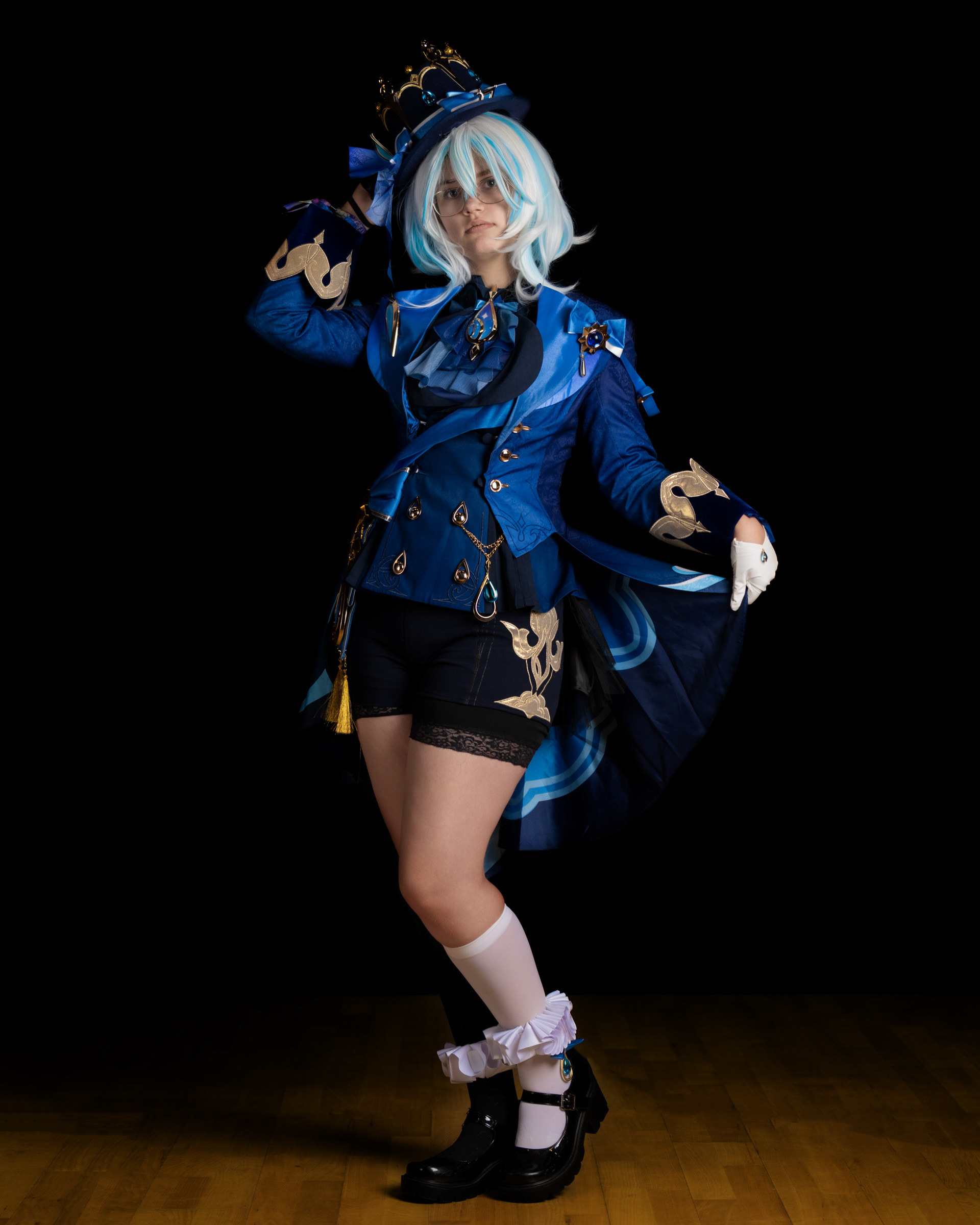 Cosplay model dressed as Furina de Fontaine from Genshin Impact posing in detailed blue costume during studio photoshoot.
