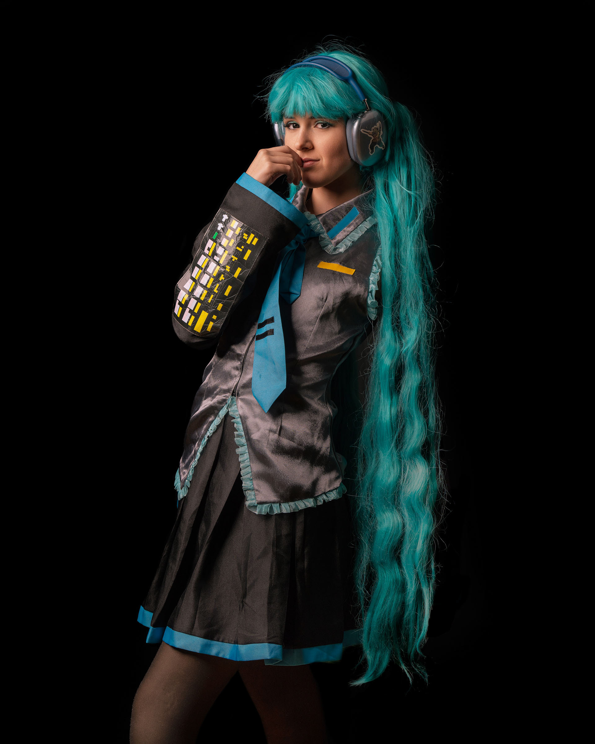 Hatsune Miku cosplayer adjusting her headphones while posing confidently, showcasing detailed arm sleeves and blue wig.