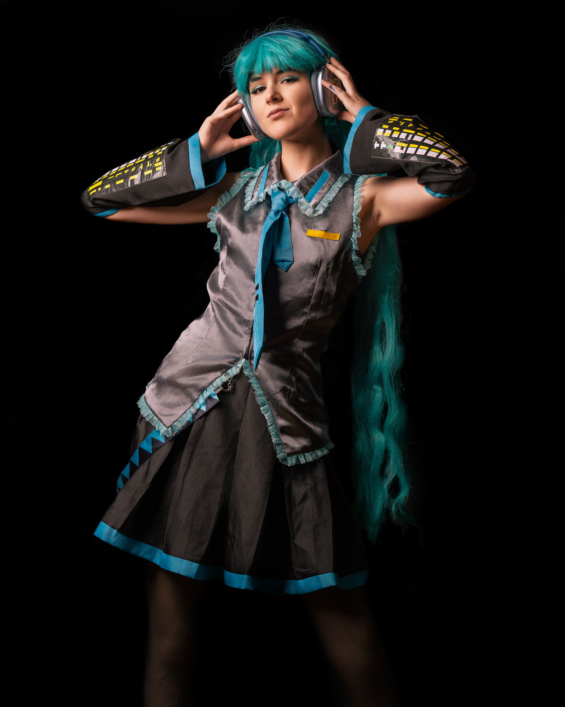 Portrait of a Miku cosplayer with long turquoise hair posing with headphones, wearing the classic Vocaloid-inspired outfit.