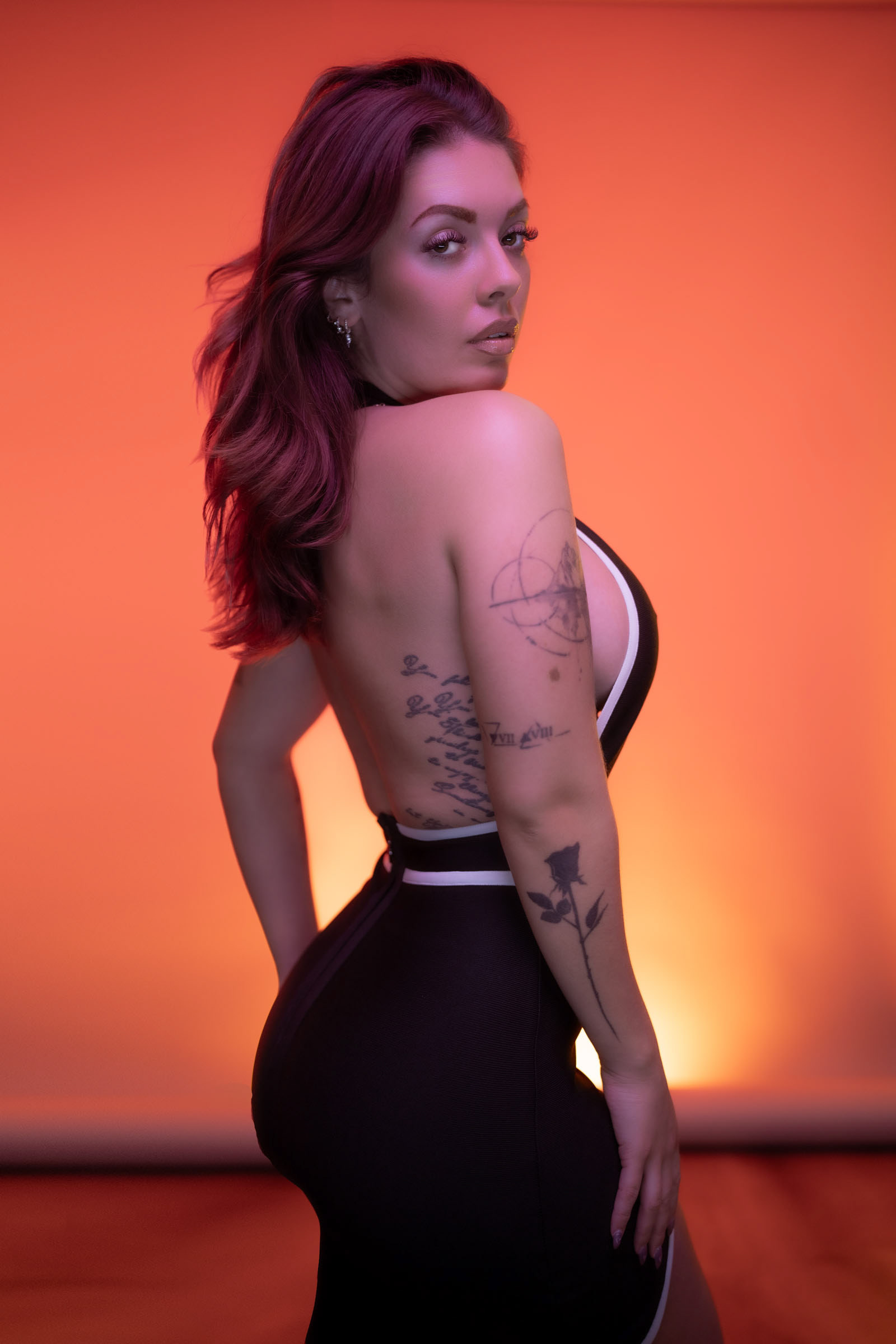 Confident female model in black and white dress posing against an orange backdrop during a fashion photo shoot with Nanlite LED lighting.