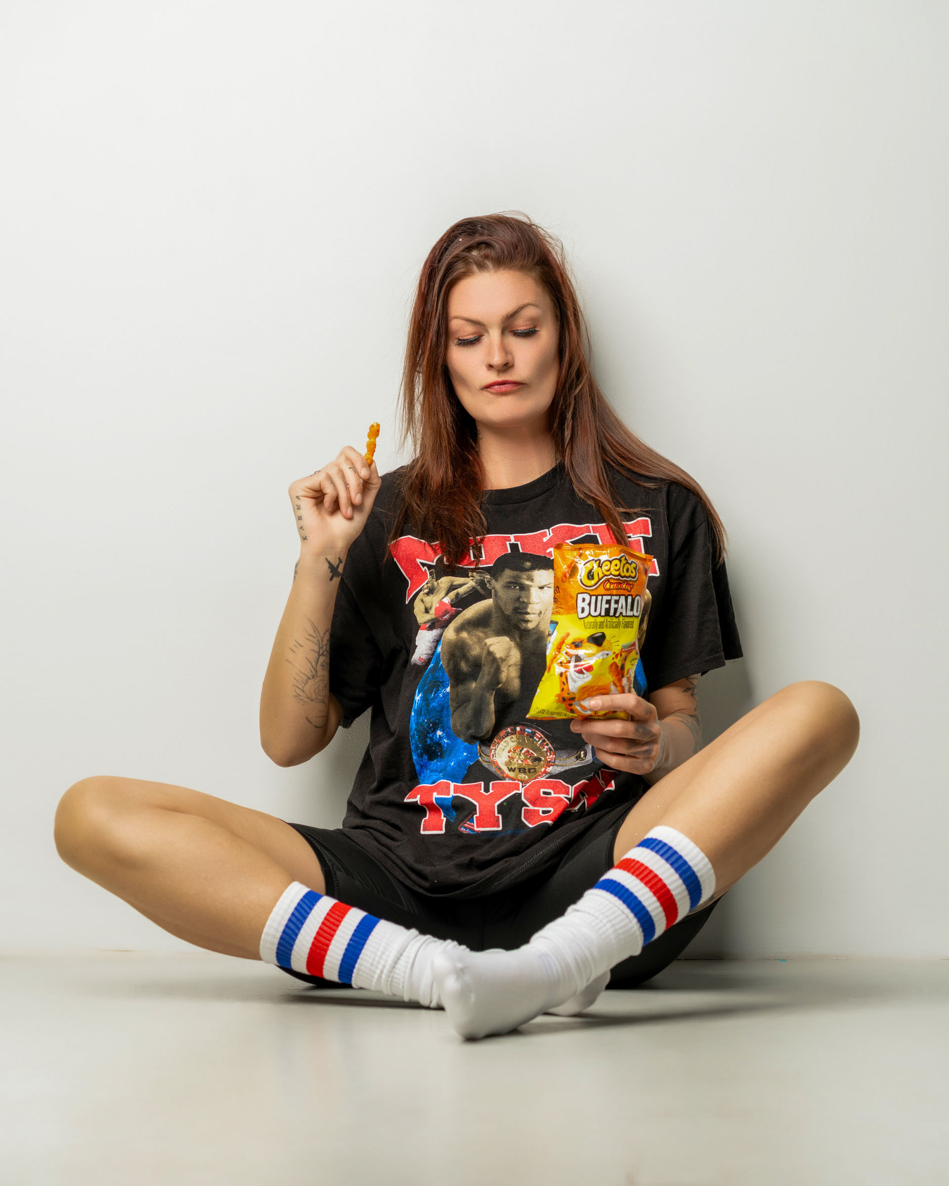 Model holding a bag of Cheetos and examining a snack piece in a playful, laid-back studio scene.