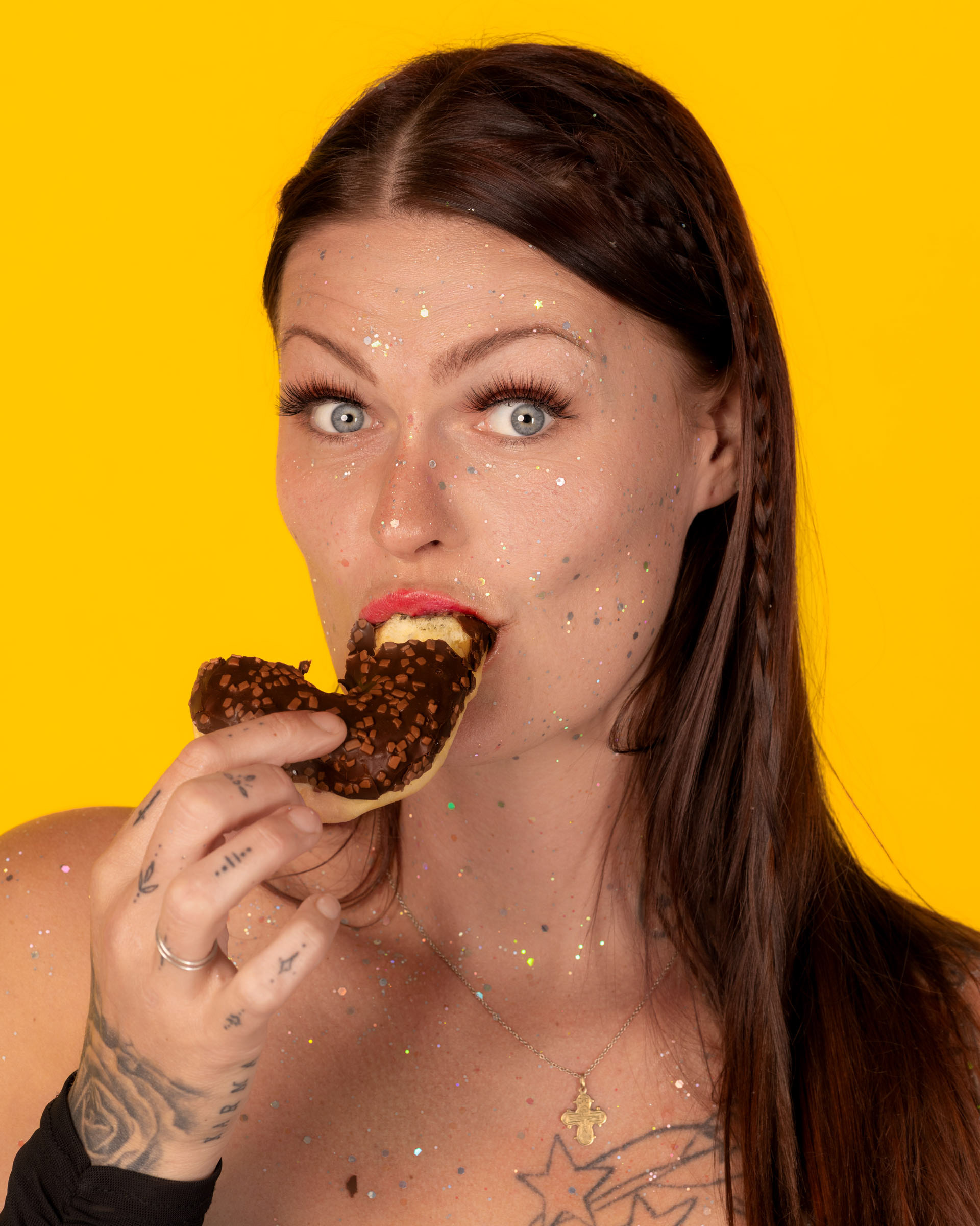 Fashionable donut-themed portrait featuring a woman in a black dress posing against a bold yellow background.