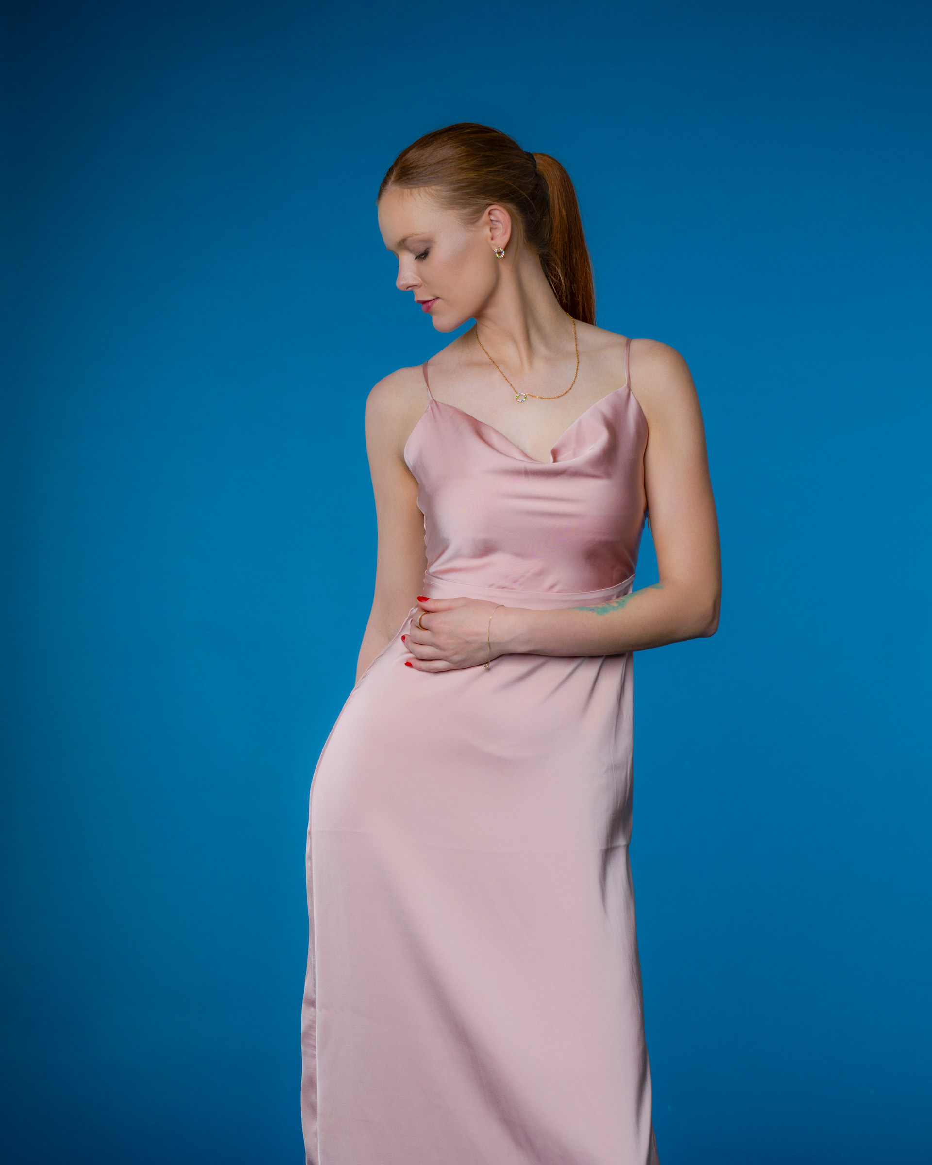 Studio portrait of model Noamynte in elegant pink dress against blue background