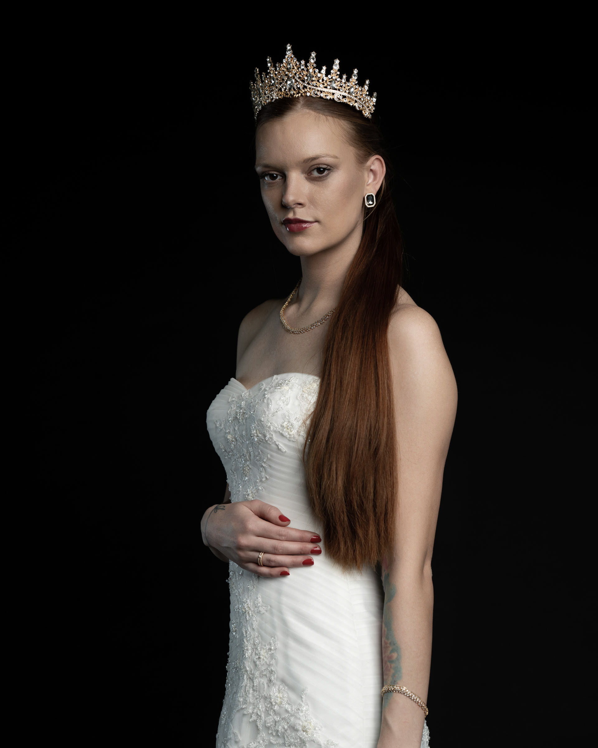 Side-lit close-up of Noamynte with a focused expression, golden crown and long hair styled neatly.