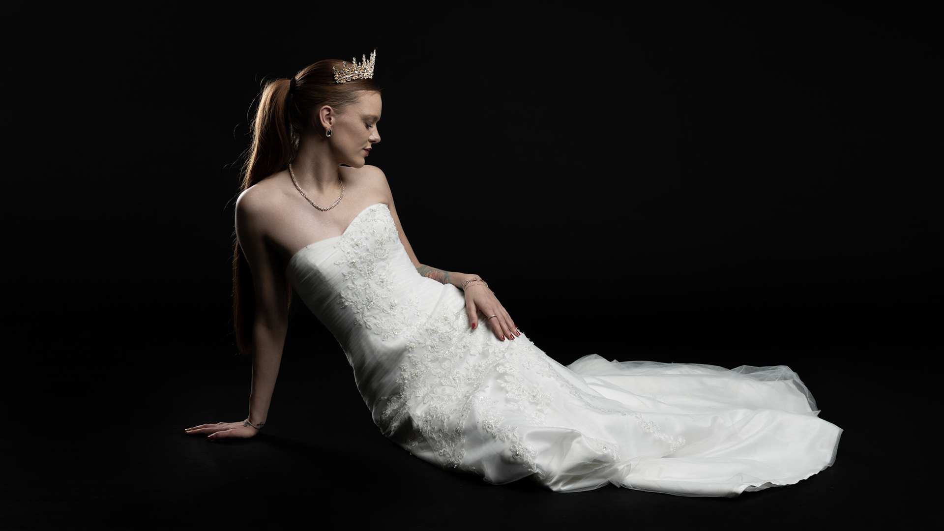 Noamynte reclining on the floor in her bridal gown, with soft lighting and royal elegance.