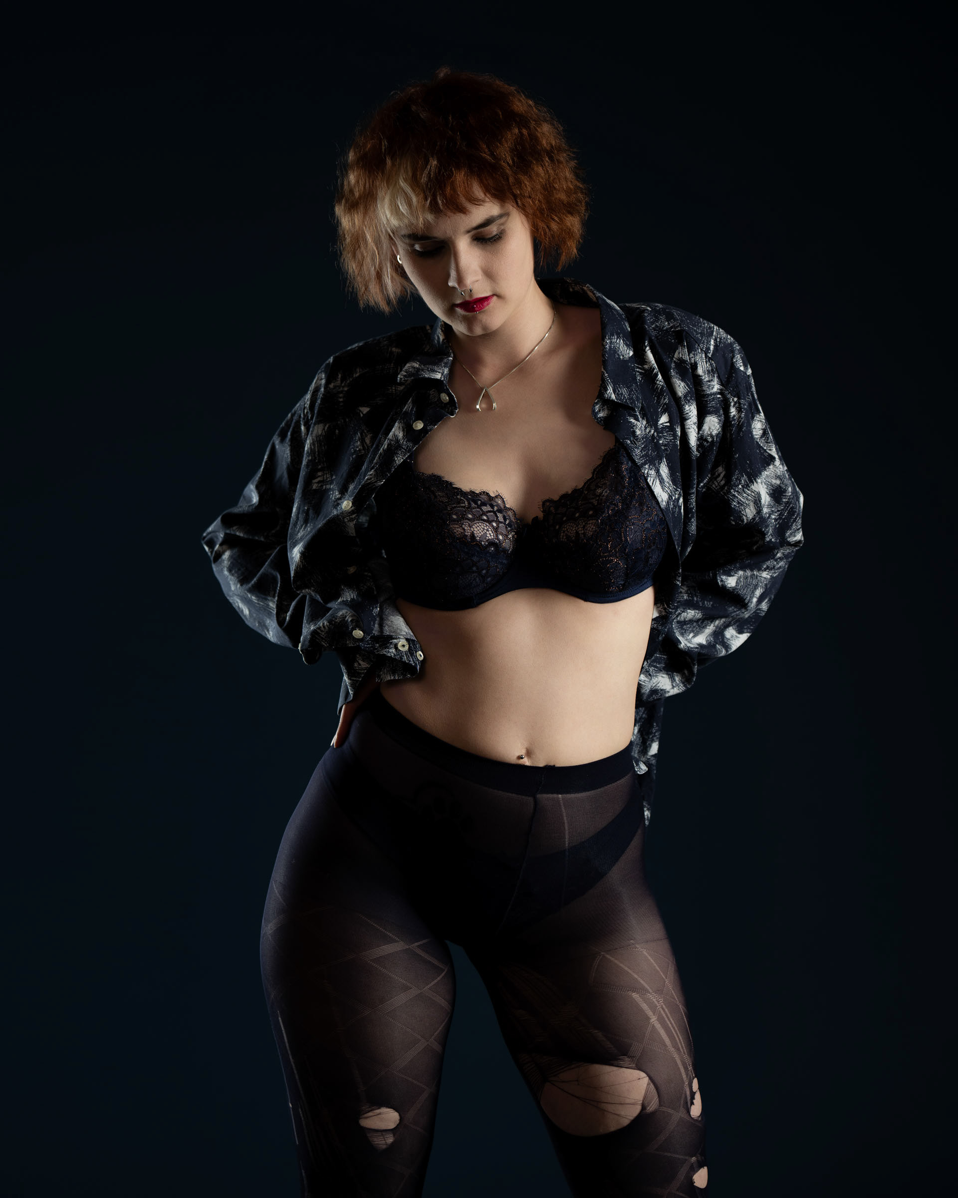 Close-up of Sisse with lace bra and printed shirt, exuding confidence and style in dramatic lighting.