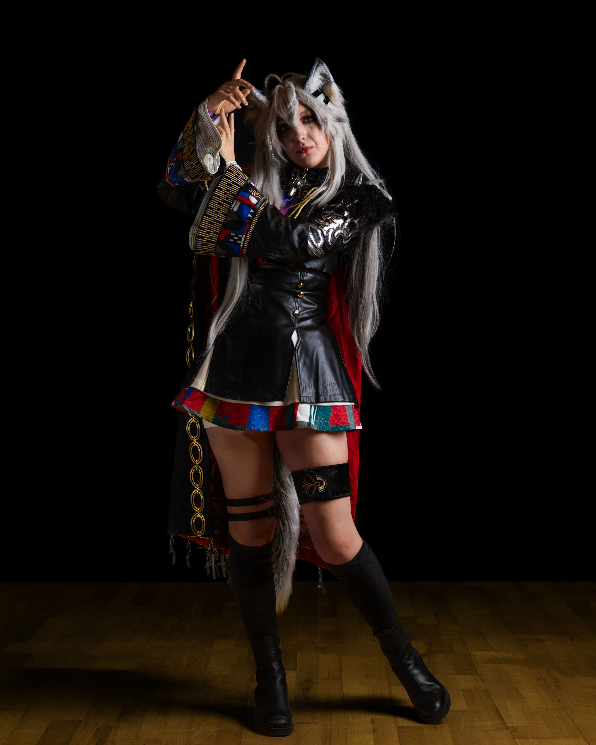 Cosplayer nether_cos dressed as Lappland from Arknights, posing in a dramatic full-body stance with a black and colorful outfit, long silver hair and wolf ears against a dark background.