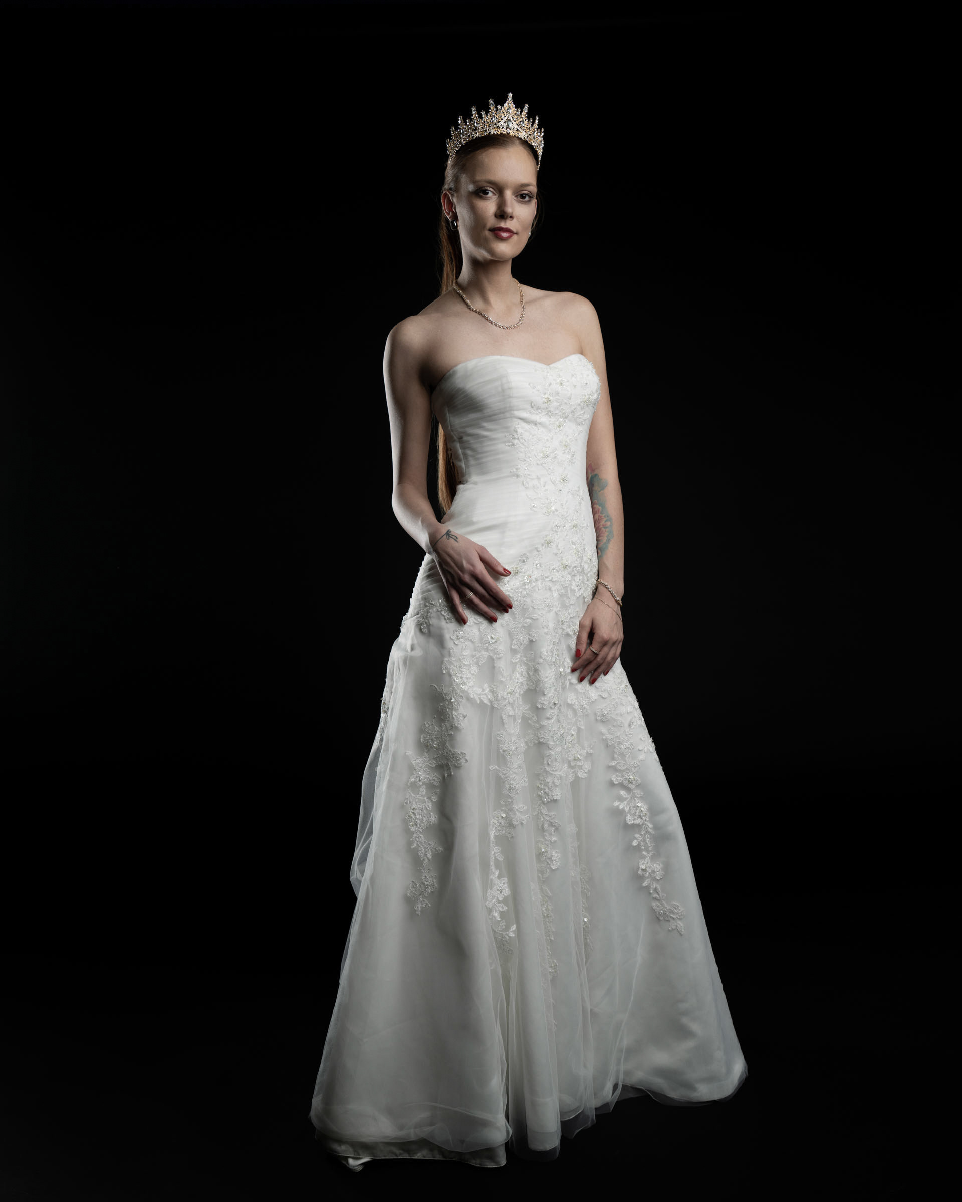 Full-body studio shot of Noamynte in a wedding dress, standing confidently with a relaxed hand on her hip.