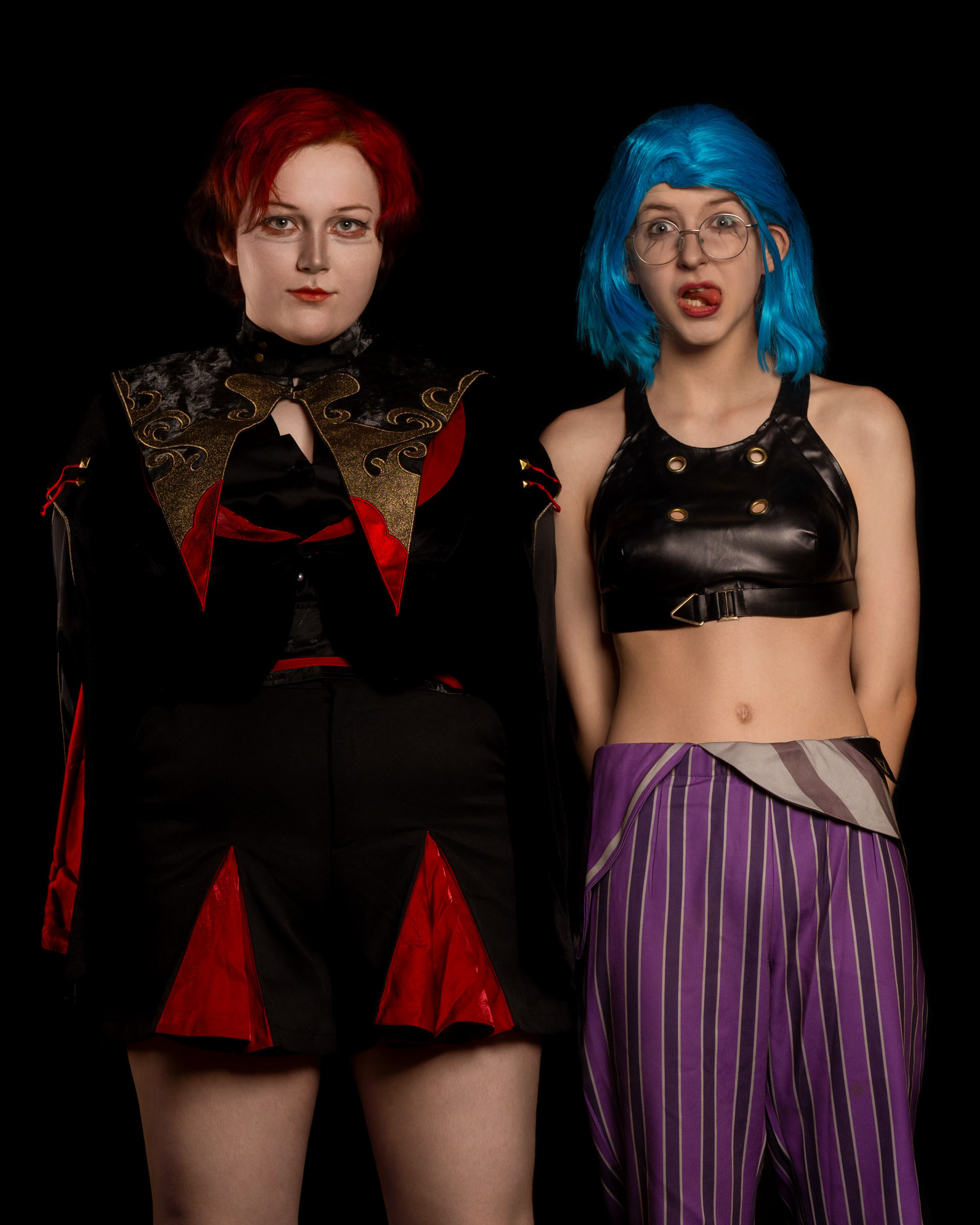 Cosplayer zen.c0z standing beside cosplayer emsc.osplay, posing together against a black background.