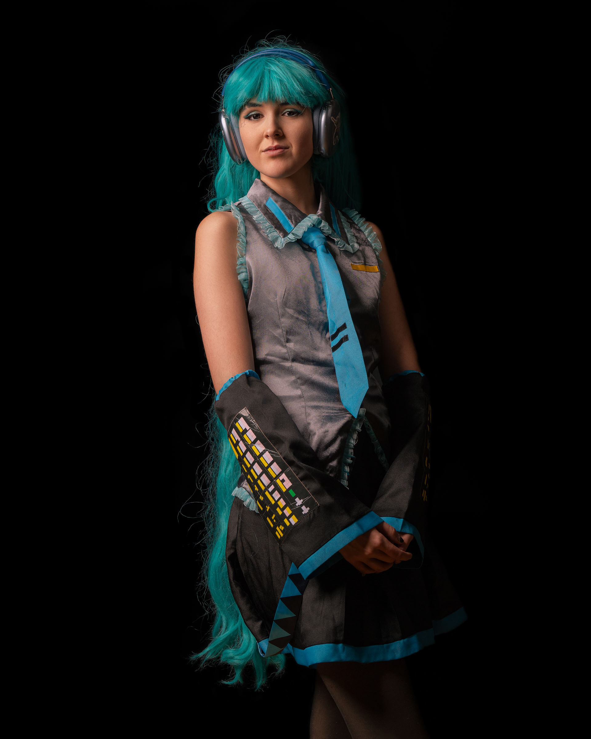 Miku cosplayer posing thoughtfully with hand near her face, emphasizing vibrant wig and patterned sleeves.