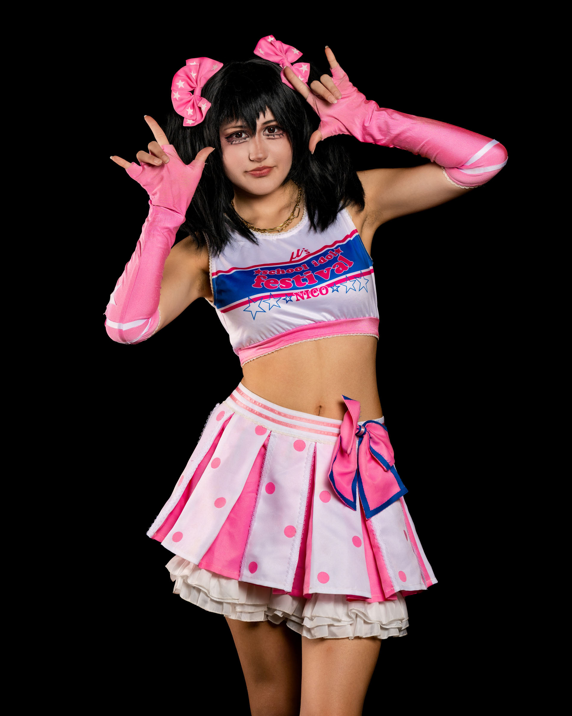 Studio portrait of may_c0z in full Nico Yazawa outfit, smiling softly while holding a pose with both hands near her face.