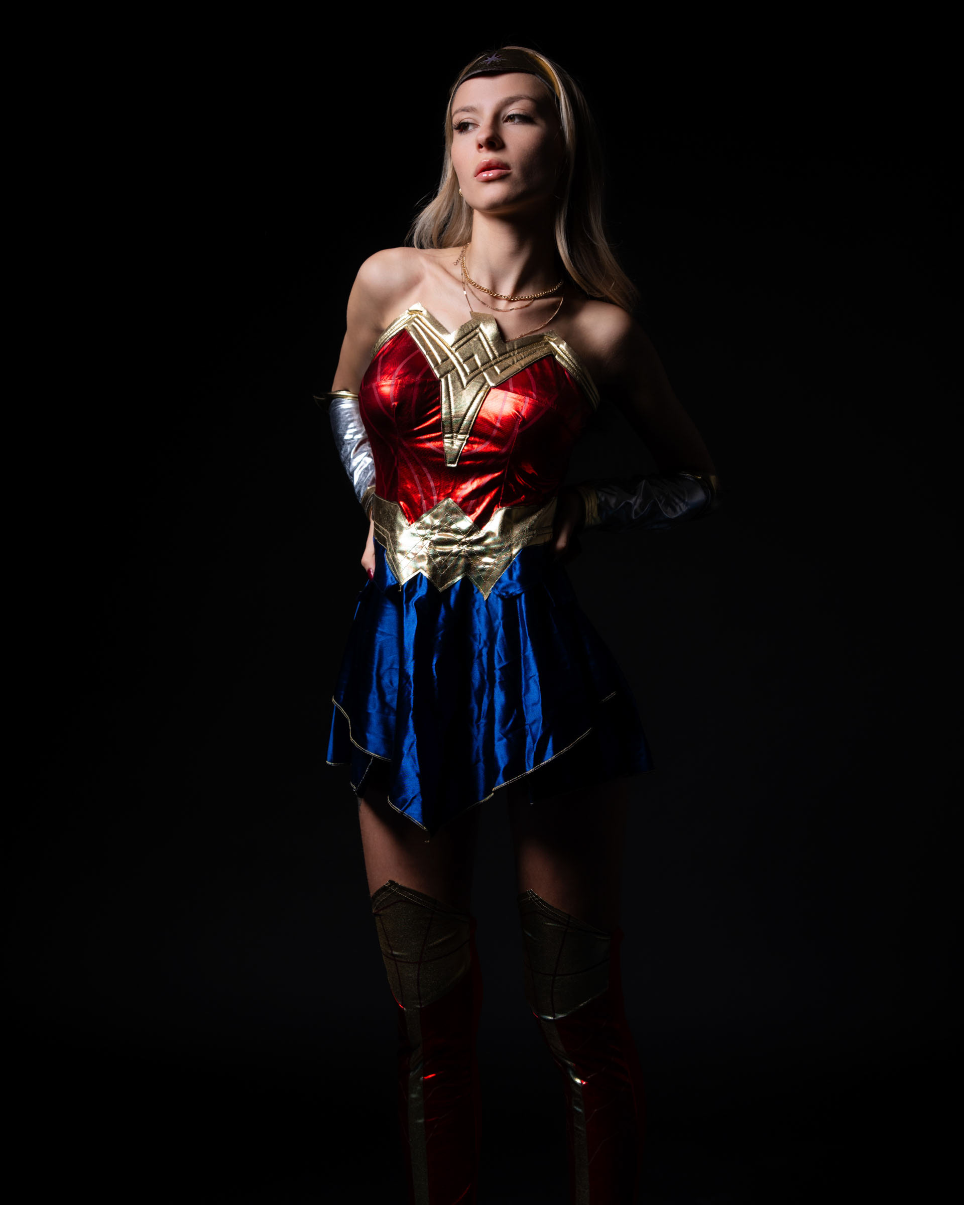 Model dressed as Wonder Woman posing confidently in low-key heroic lighting.