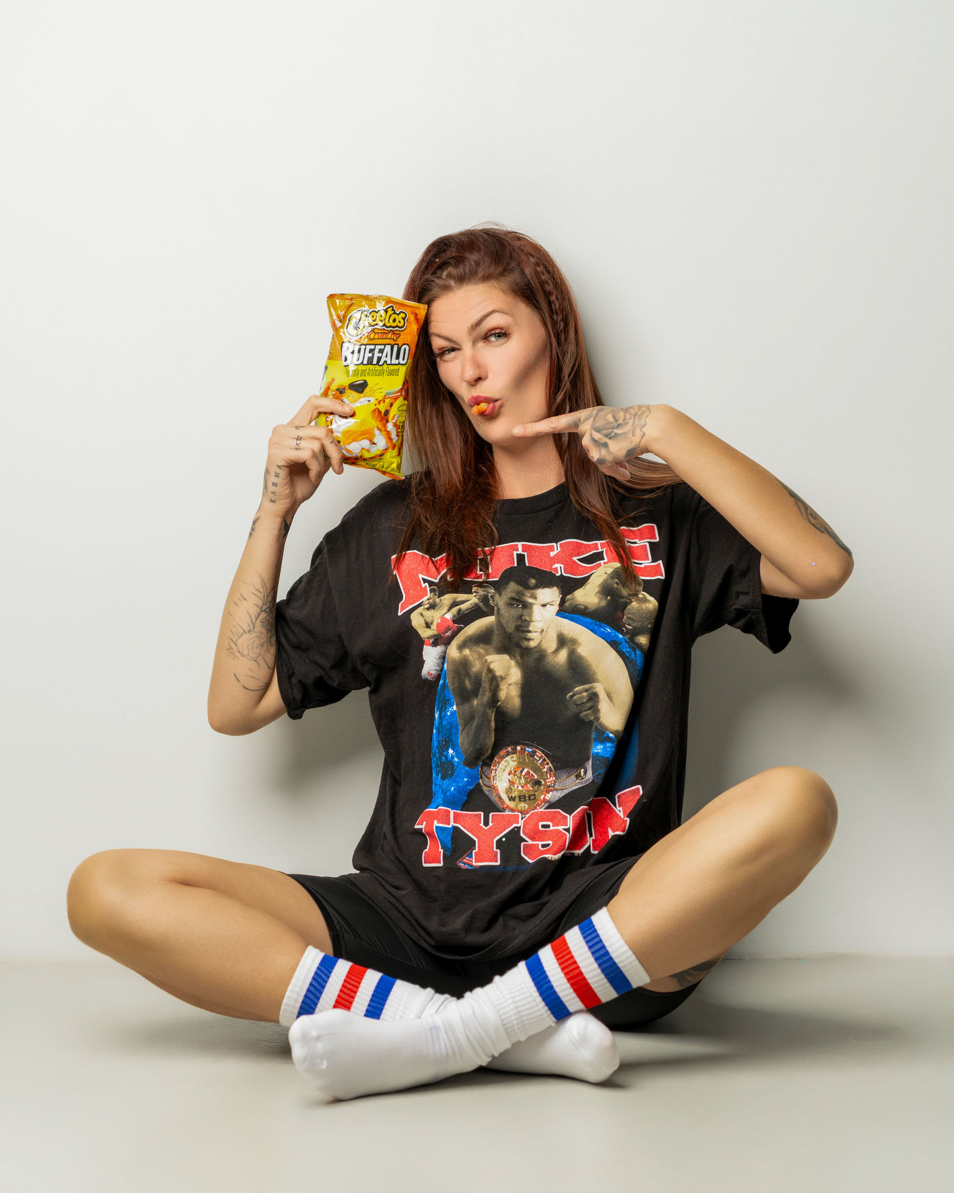 Chill lifestyle portrait of a woman in a graphic T-shirt enjoying a cheese snack against a minimal white background.