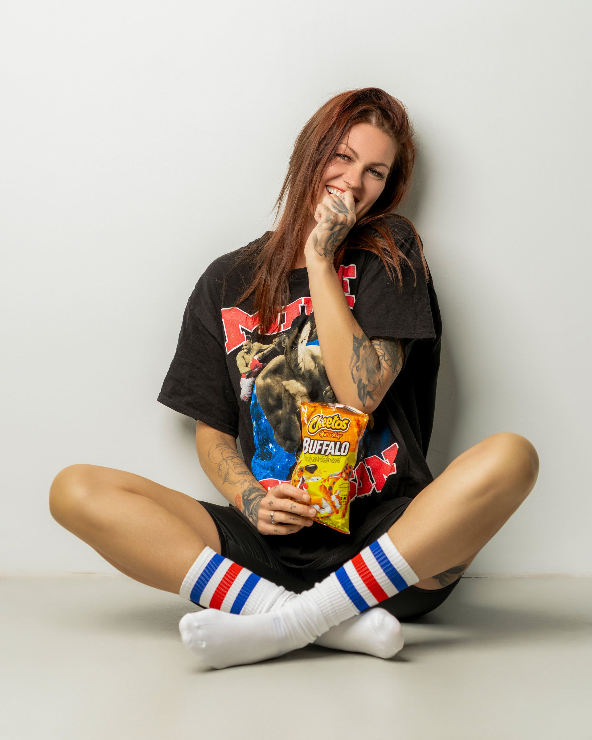 Fun and relaxed photo featuring a model sitting cross-legged with a bag of Cheetos and a curious expression.