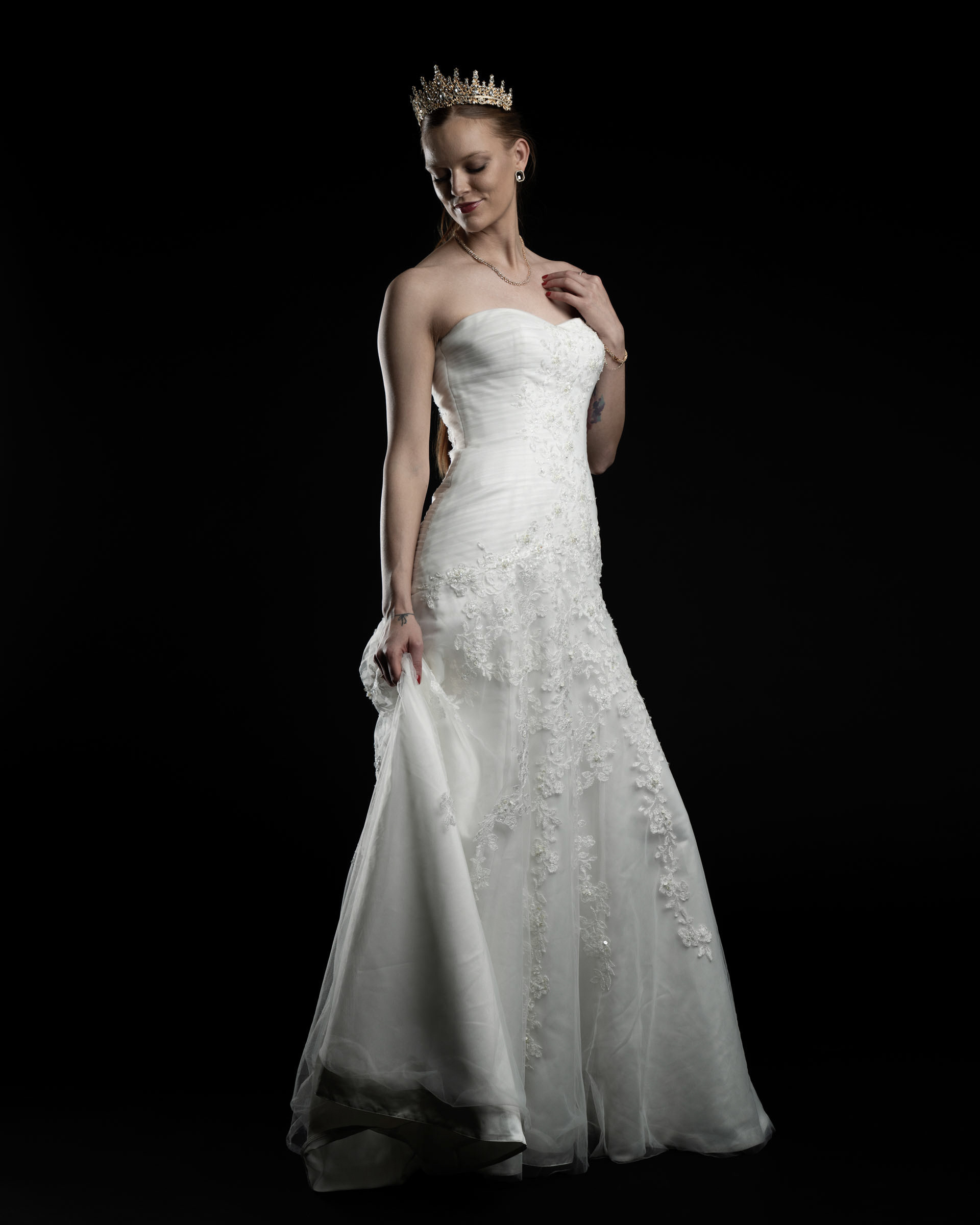 Noamynte gently holding her dress, looking to the side in a soft and romantic bridal pose.