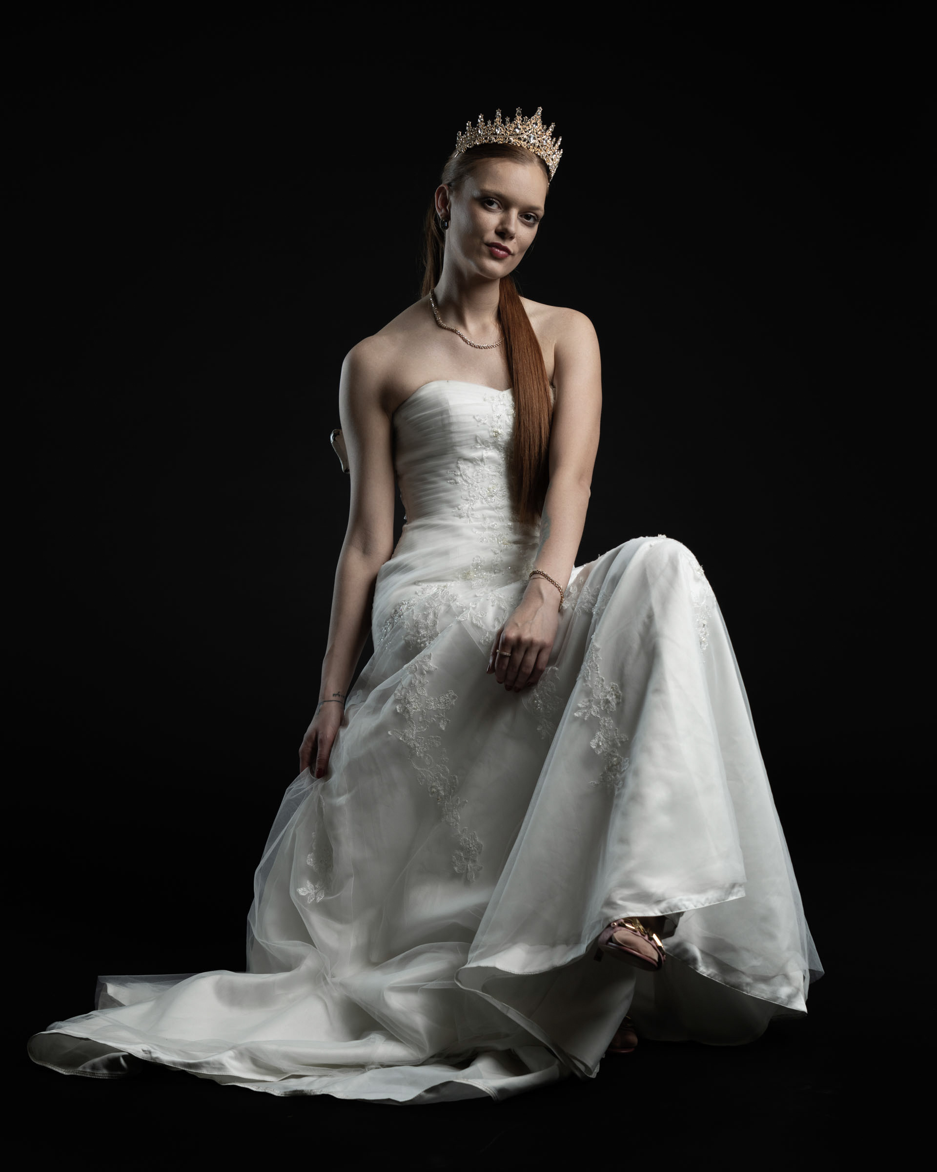 Seated studio portrait of Noamynte with one knee up, showcasing the dress’s flow and her confident gaze.