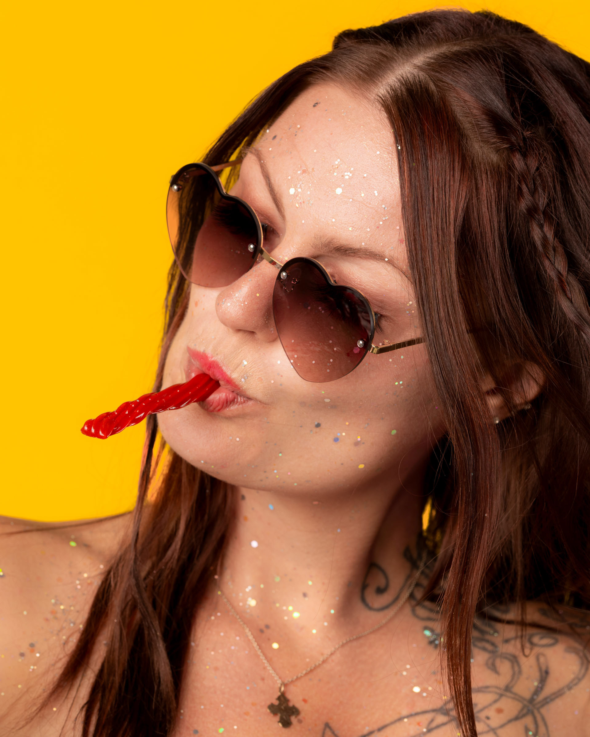 Model holding a candy bag and playfully licking a red Twizzler in a bold, colorful portrait setup.