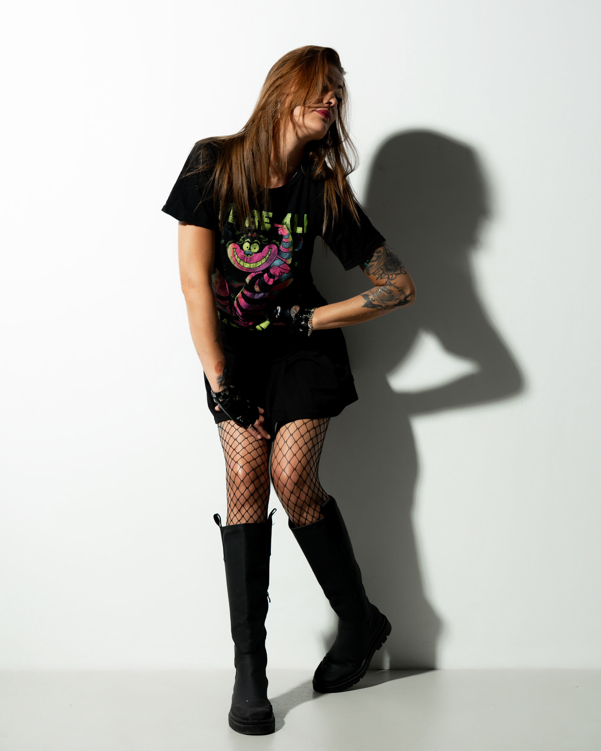 Simone leaning sideways with one hand on her knee, casting a strong shadow behind her against a white wall.