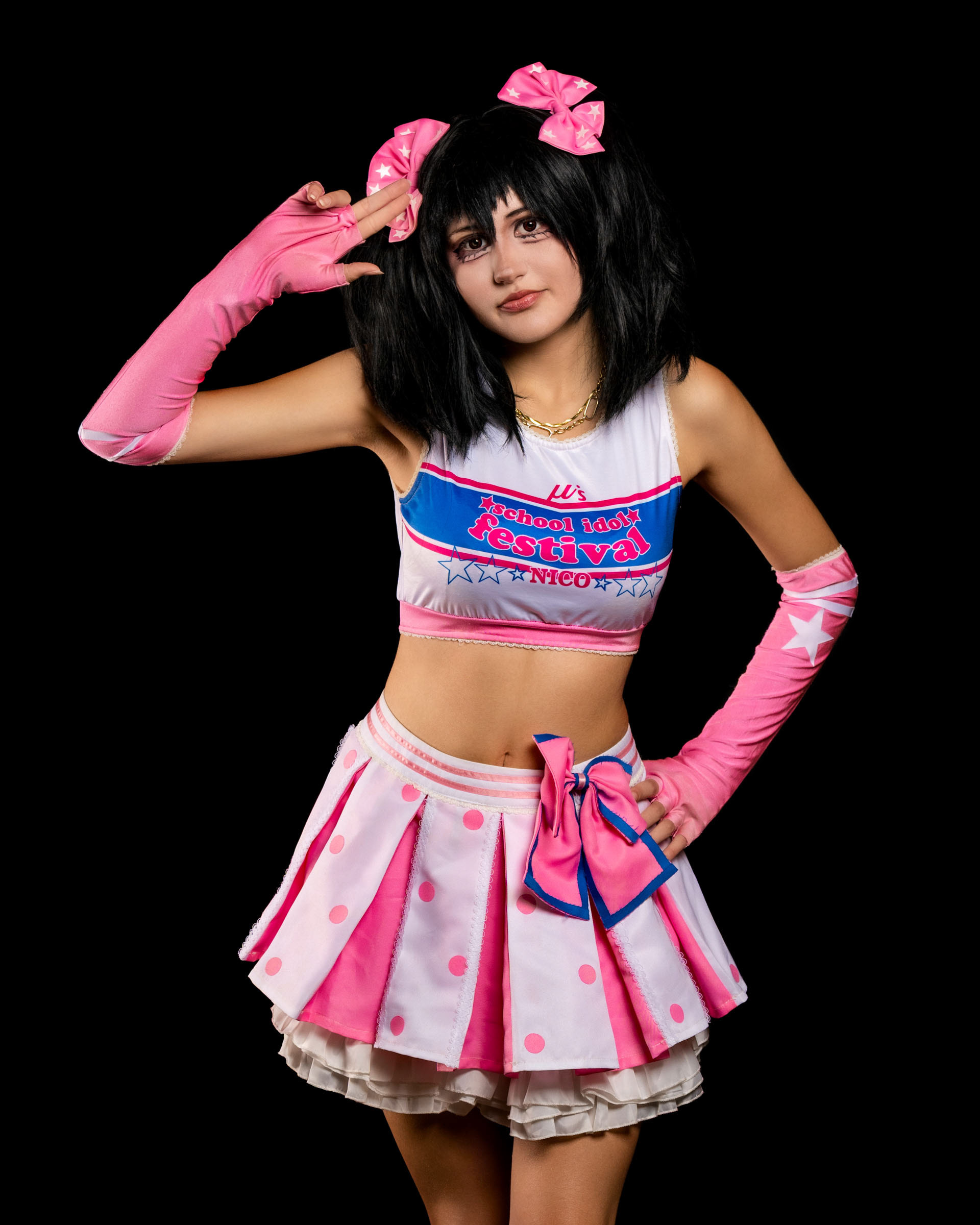 Full-body studio photo of may_c0z as Nico Yazawa striking a playful idol pose in a pink skirt and matching accessories.