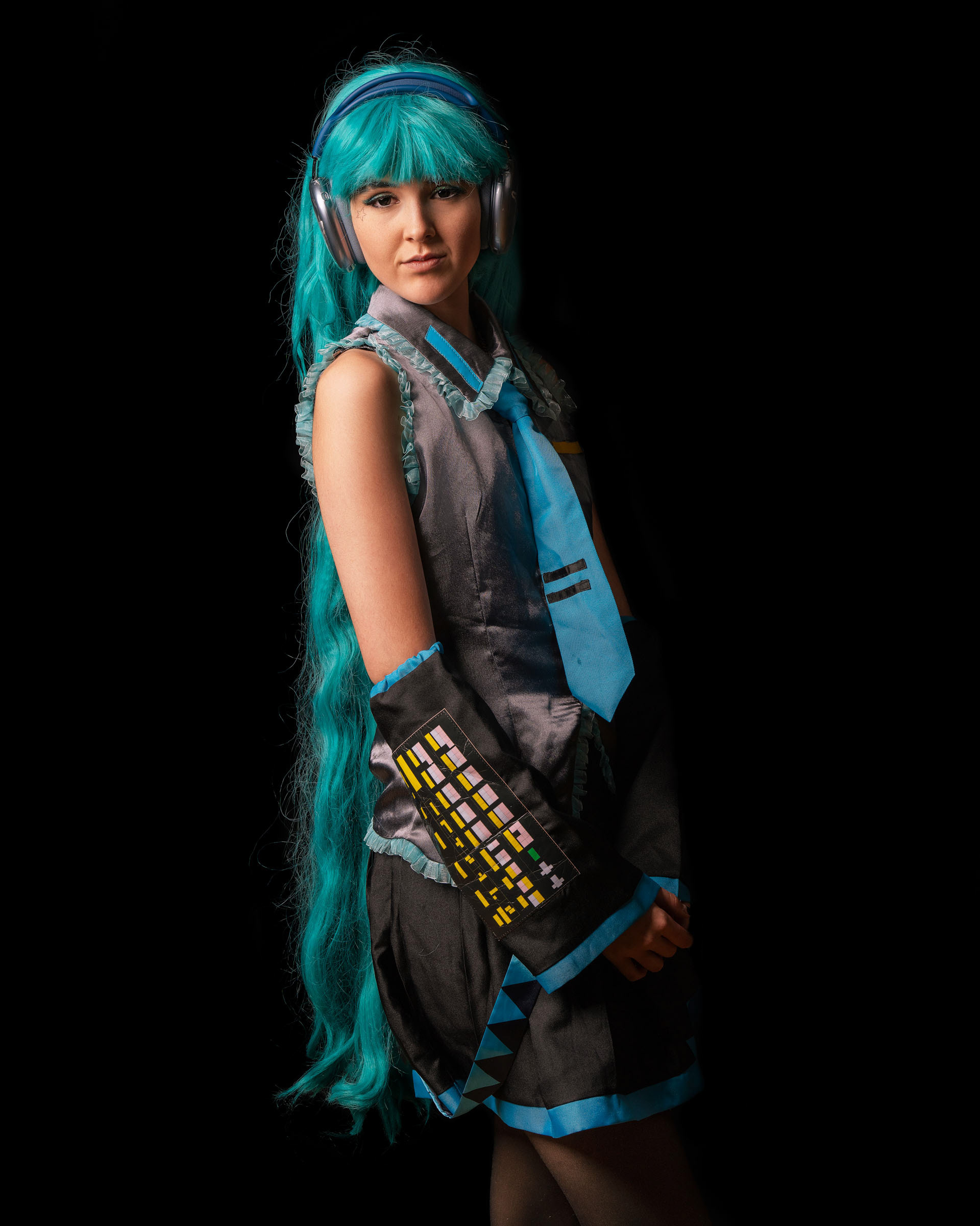 Side-angle portrait of Hatsune Miku cosplay, highlighting the long turquoise wig and futuristic character design.