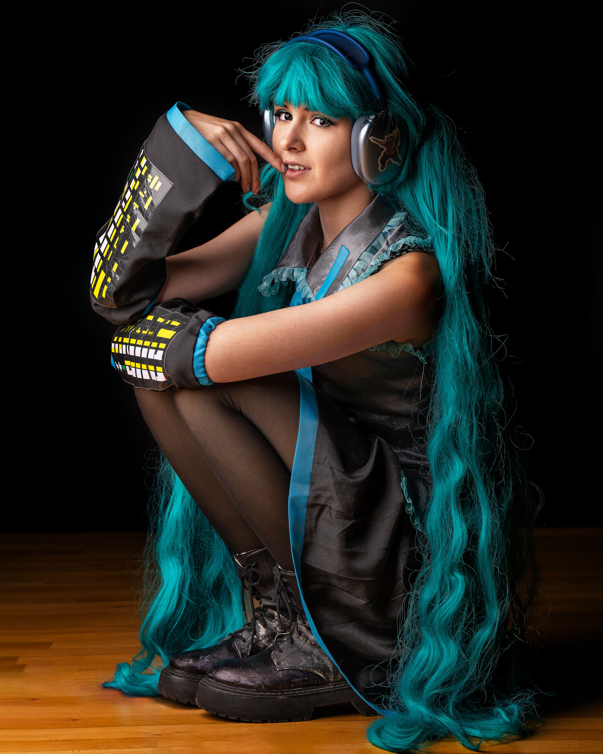 Close-up portrait of Miku cosplayer sitting and posing with a playful expression, highlighting wig texture and costume details.