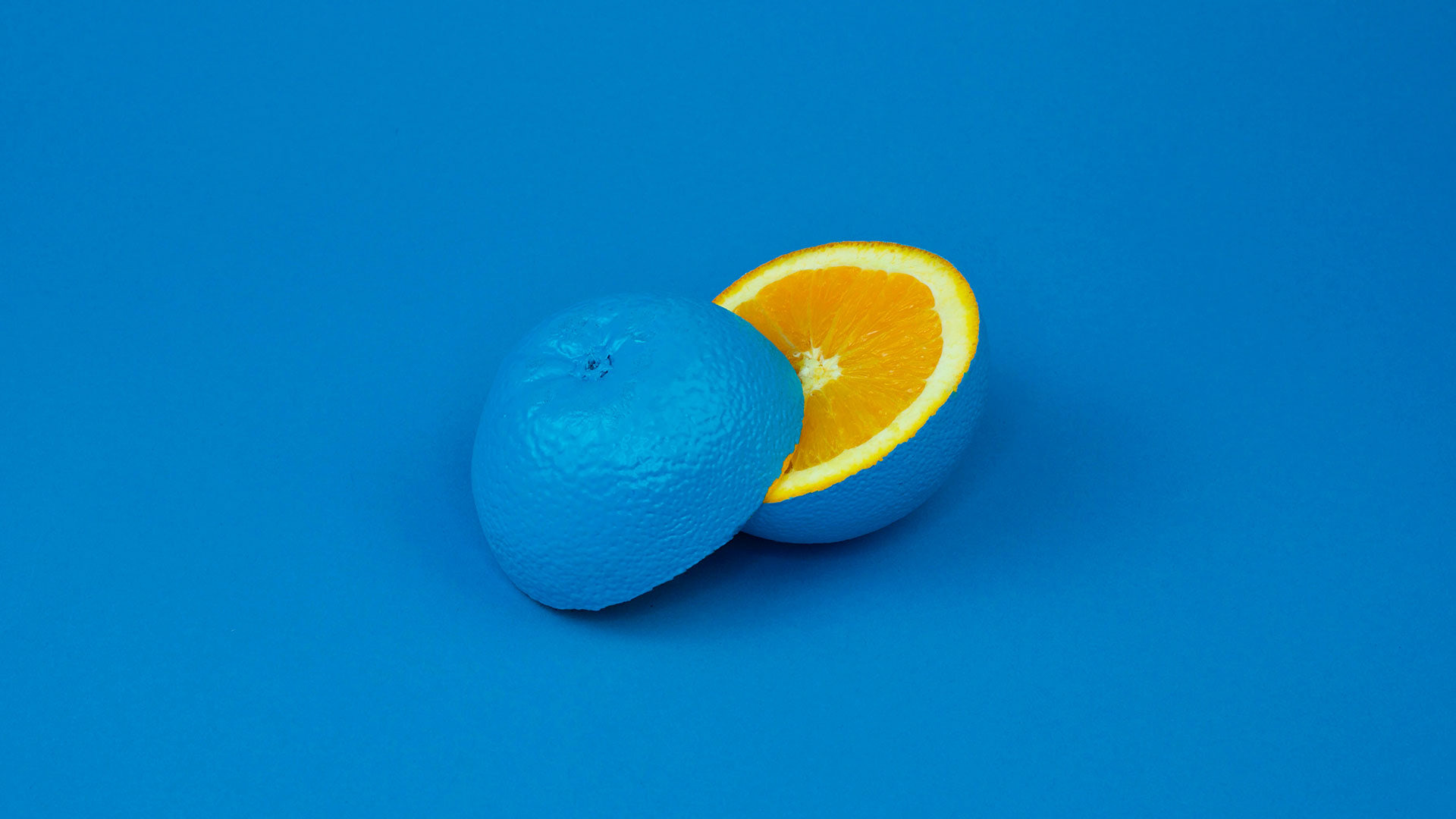 Bright blue background with a halved orange, painted and centered.