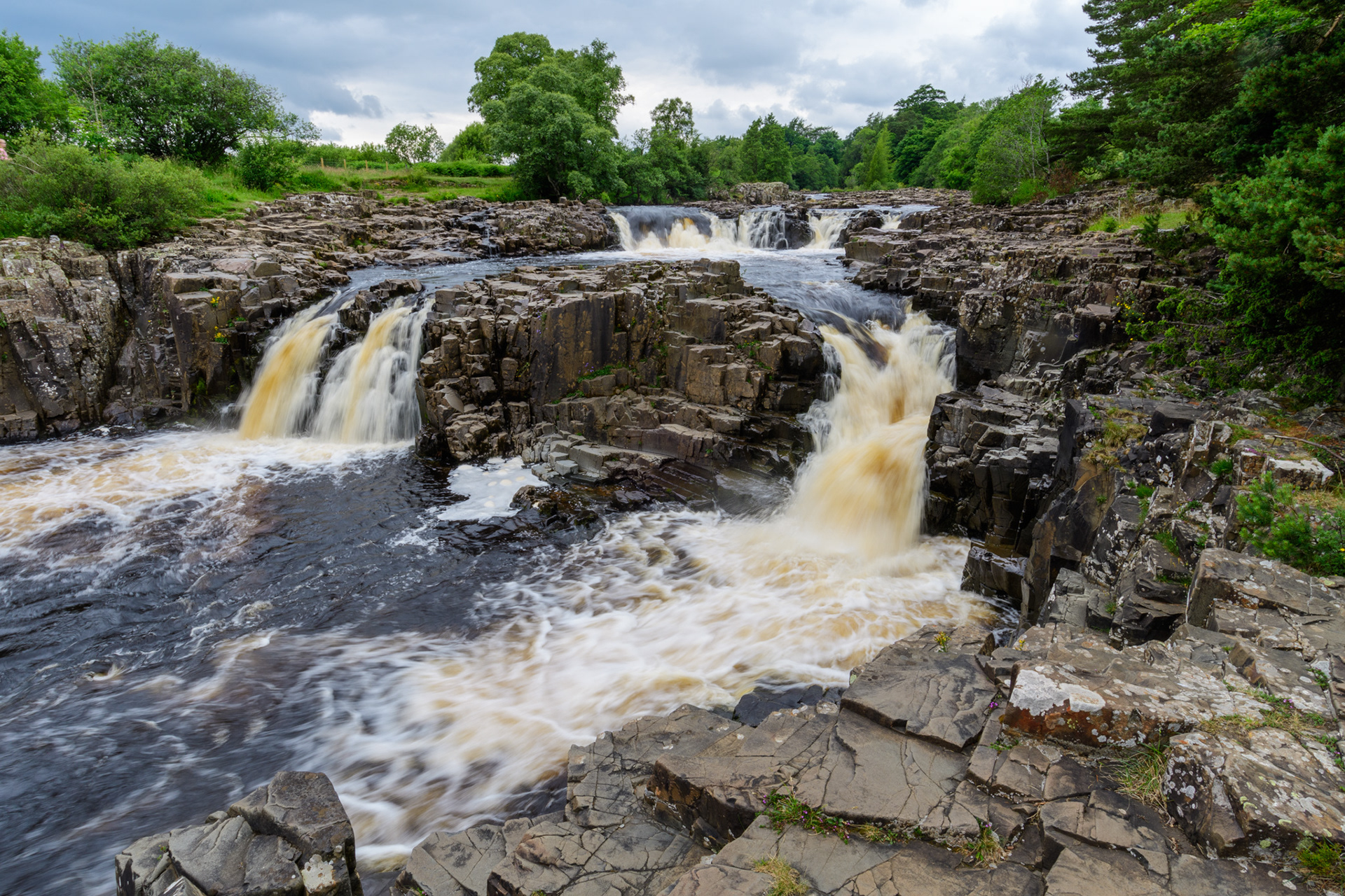 A summer time view of a large cascade flowing over hard, angular granite rocks