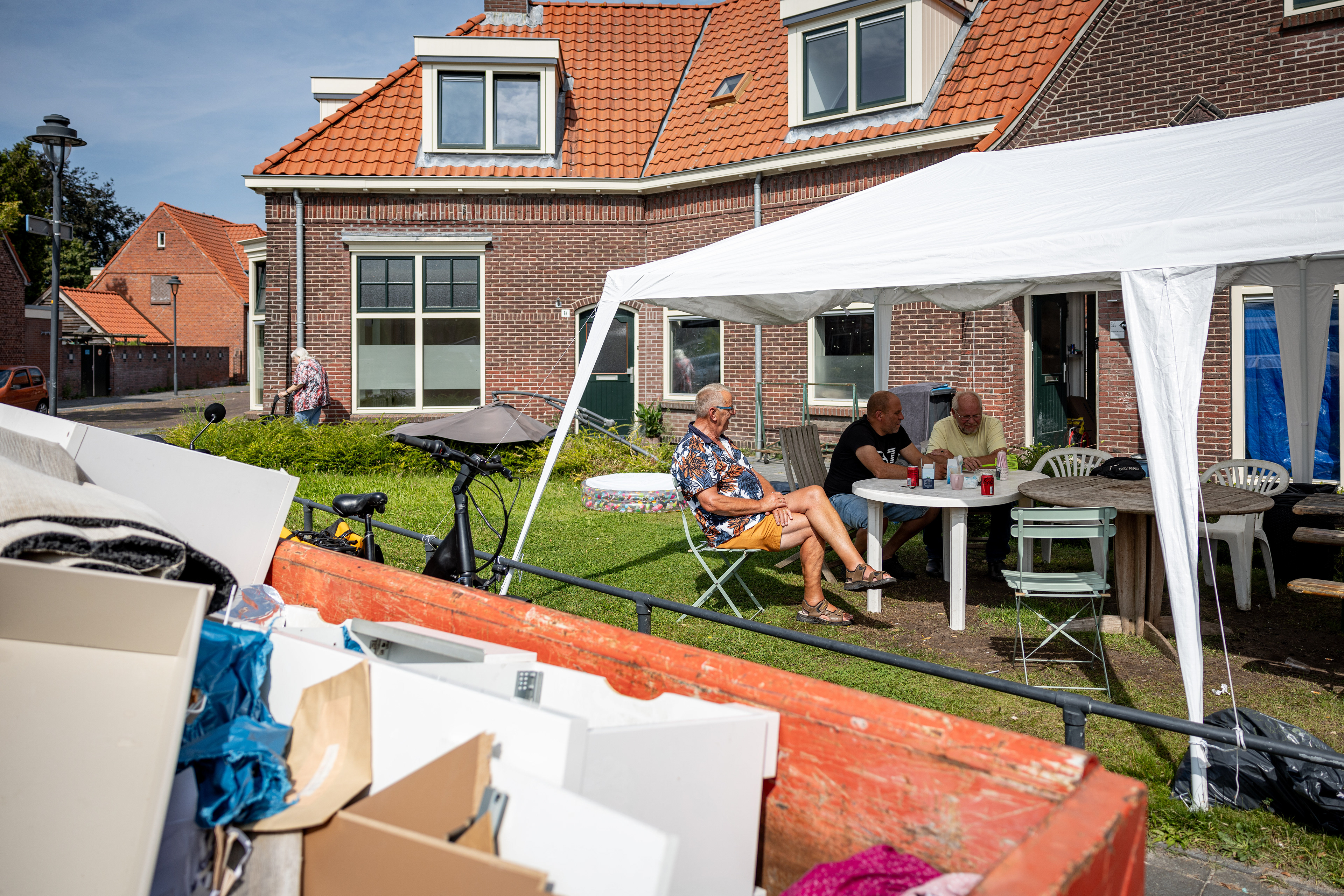 Bewoners van de Enschedese wijk Pathmos zitten onder een partytent op een plantsoen in hun wijk. Wat lijkt op een buurtfeest is het allesbehalve. Vijf weken geleden overstroomden ruim vijftig woningen met regen- en rioolwater na hevige buien. Veel woningen zijn onbewoonbaar verklaard.