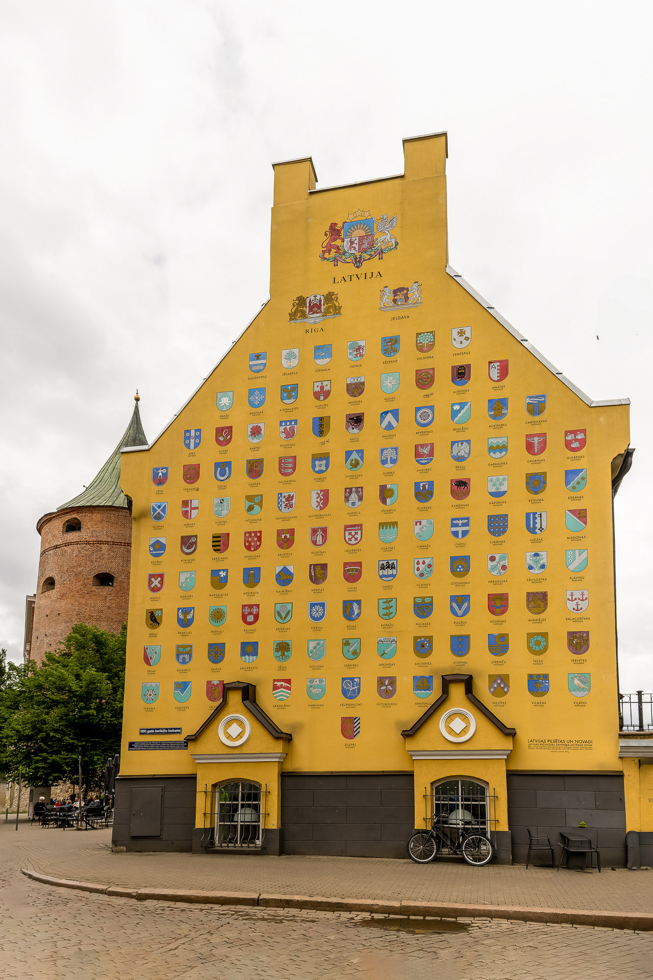 Riga - Les casernes de Jacob   : Le mur présente une immense fresque murale jaune décorée des armoiries de nombreuses villes, municipalités et régions lettones)(