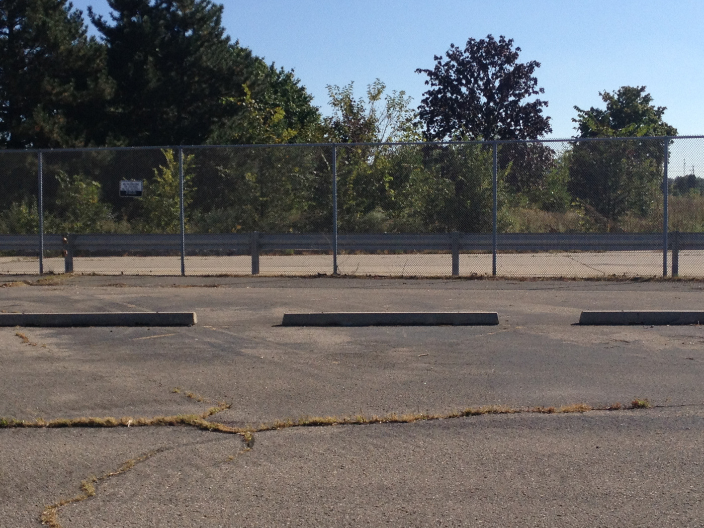 A fence separates the vacant lot of the factory and the parking lot.