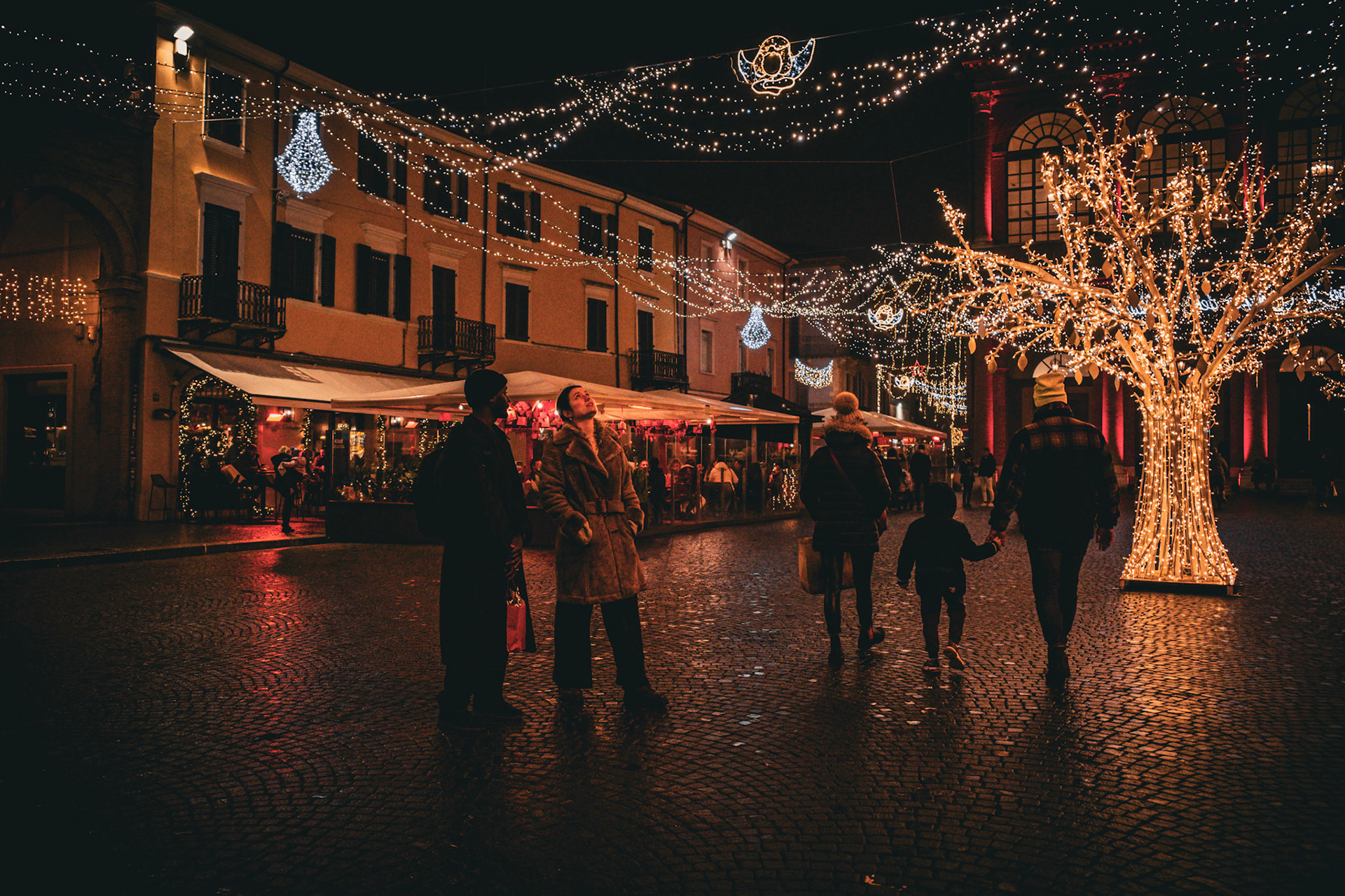 The square turns into an inverted sky, where lights descend to meet people. Footsteps slow down, gazes rise, hands search for other hands. Winter watches silently as the city allows itself a gentle illusion. For a moment, everything feels lighter: time, cold, even the future.