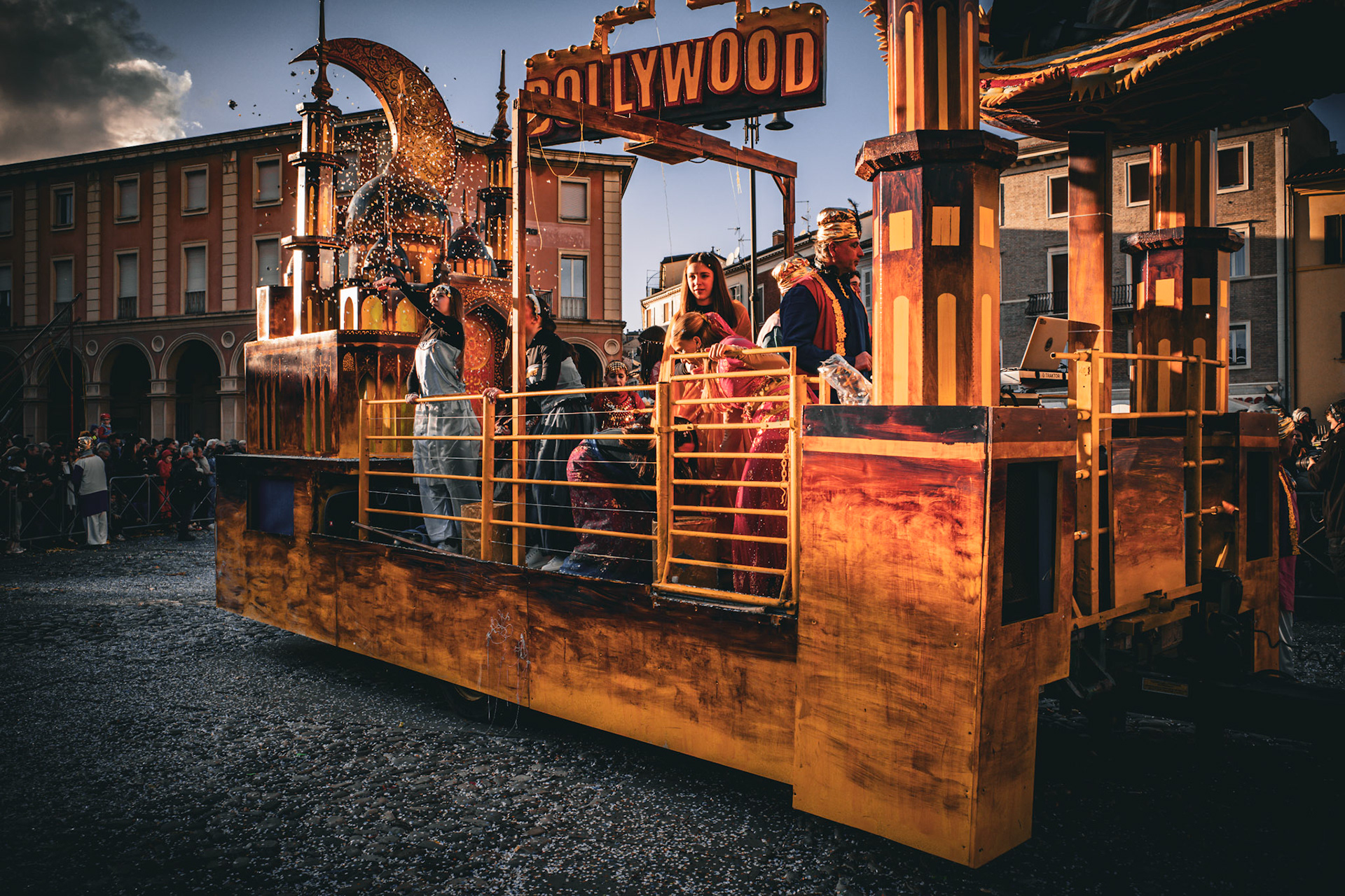 A float moves forward through confetti and gazes, carrying a handcrafted elsewhere. Gold, fabrics, and symbols dance beneath the low sun, while the crowd accepts the pact: to believe, if only for a moment. In this slow passage, the city allows itself to be crossed by a dream.