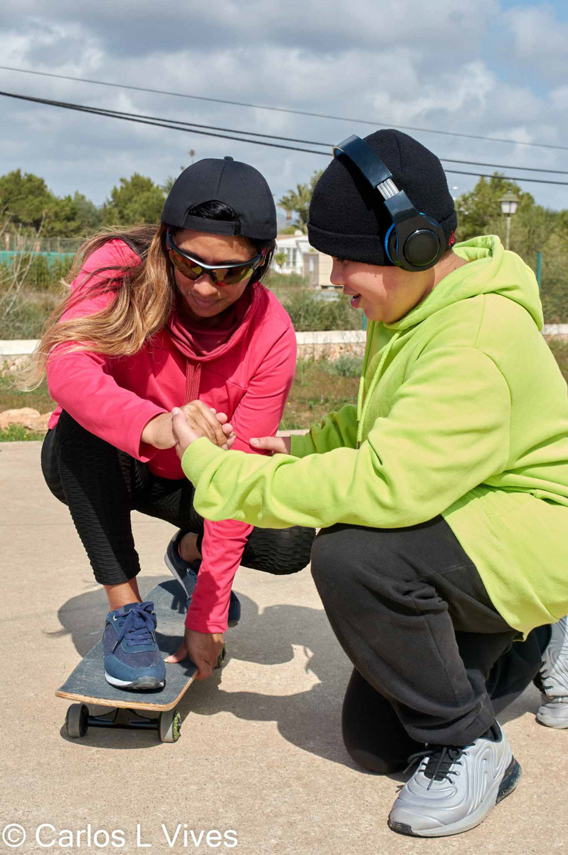 young teenager teaches and helps young latina woman how to skateboard