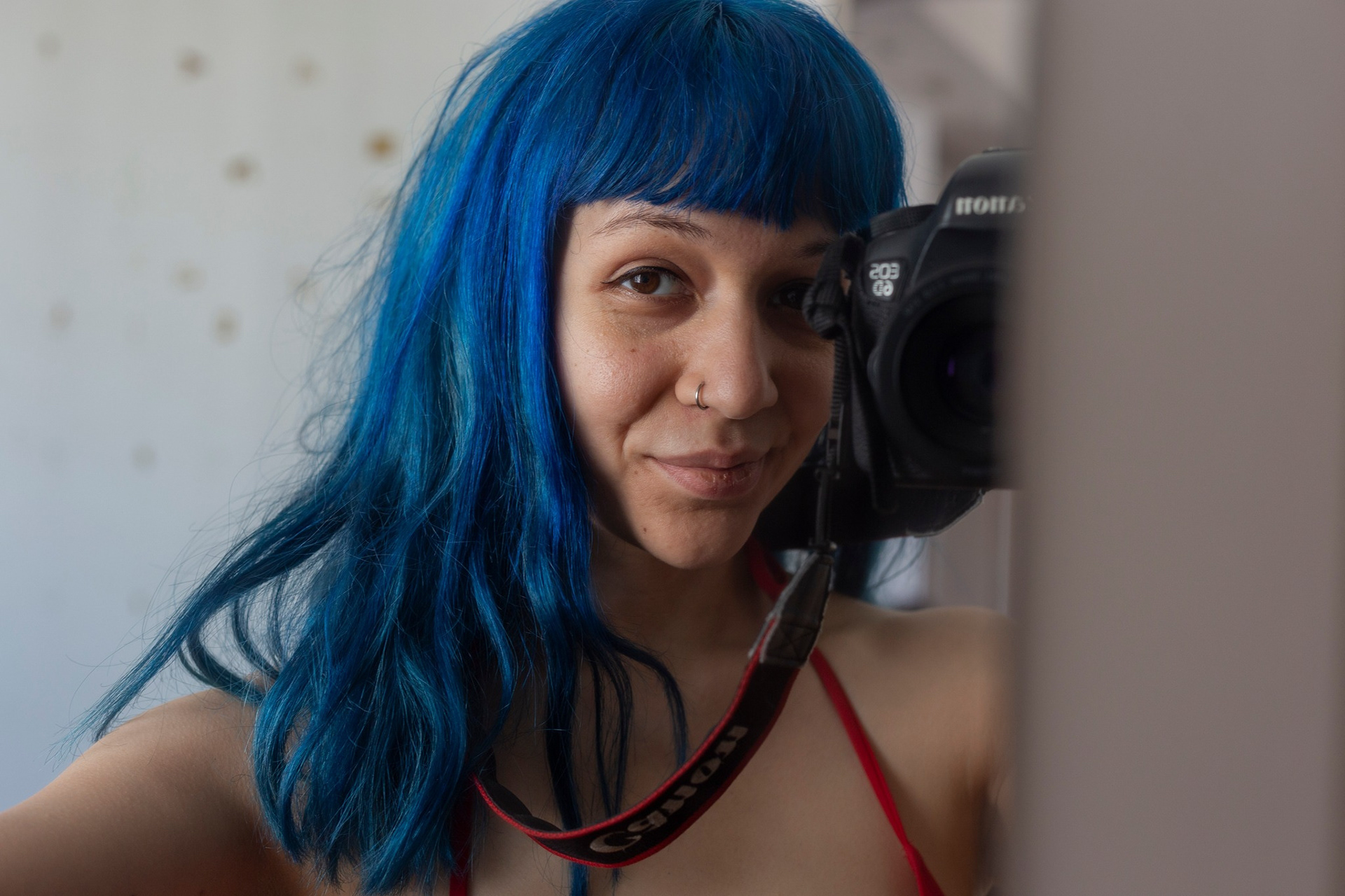 autoretrato de una mujer joven de pelo azul y ojos oscuros en frente de un espejo con una cámara digital