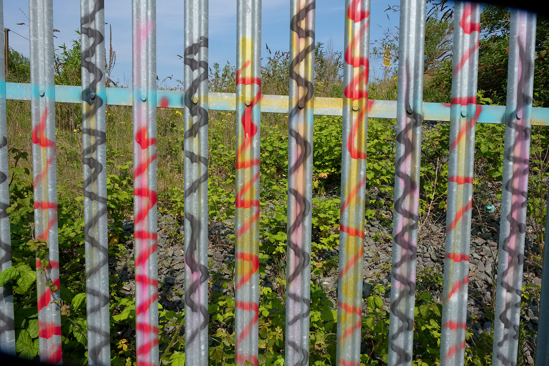 A colour photo of vertical steel fencing covered in wiggly graffiti