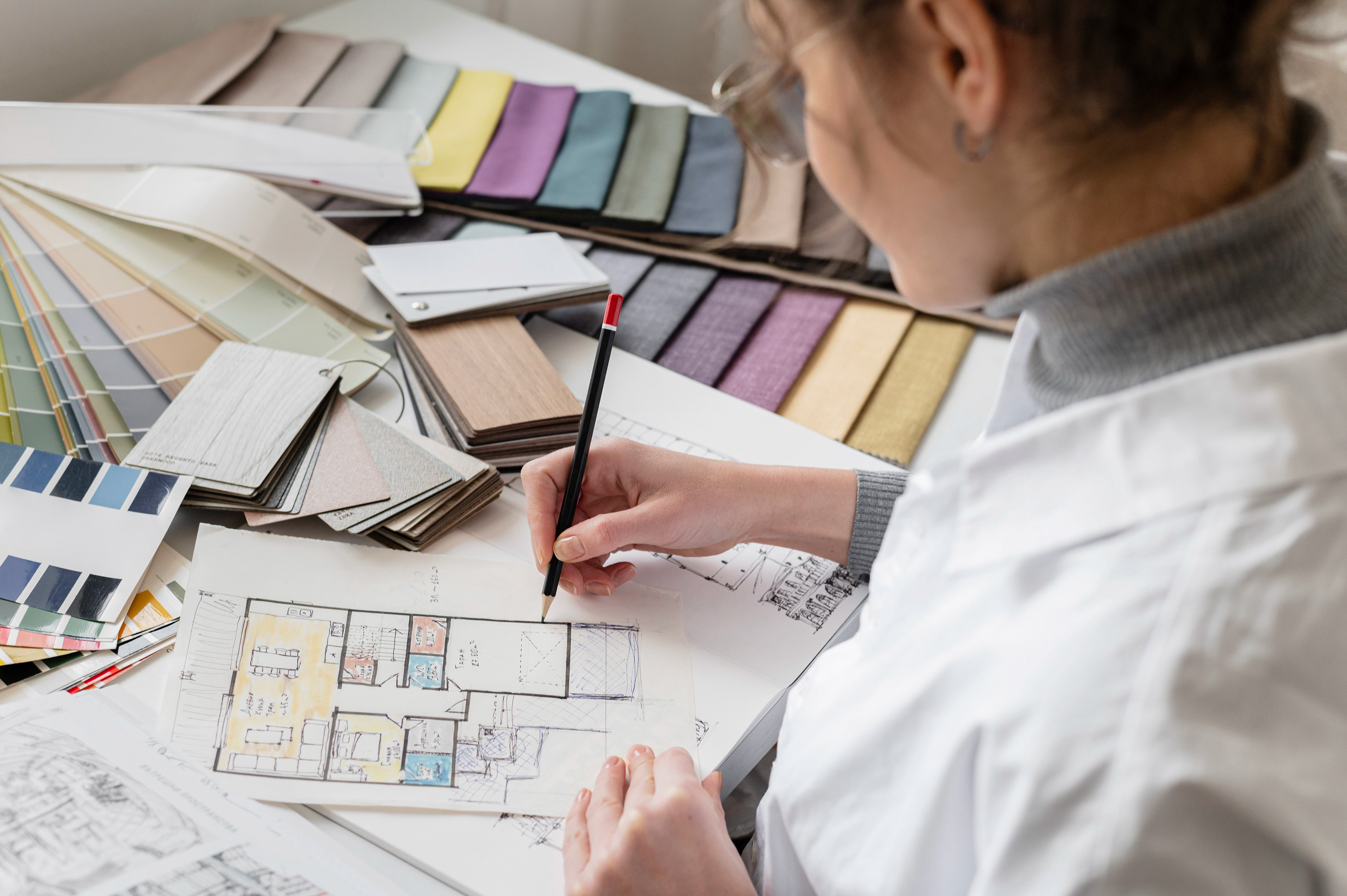 Décoratrice d'intérieur travaillant sur un plan d'aménagement de l'espace. Echantillons de textile, de matière et de peinture.