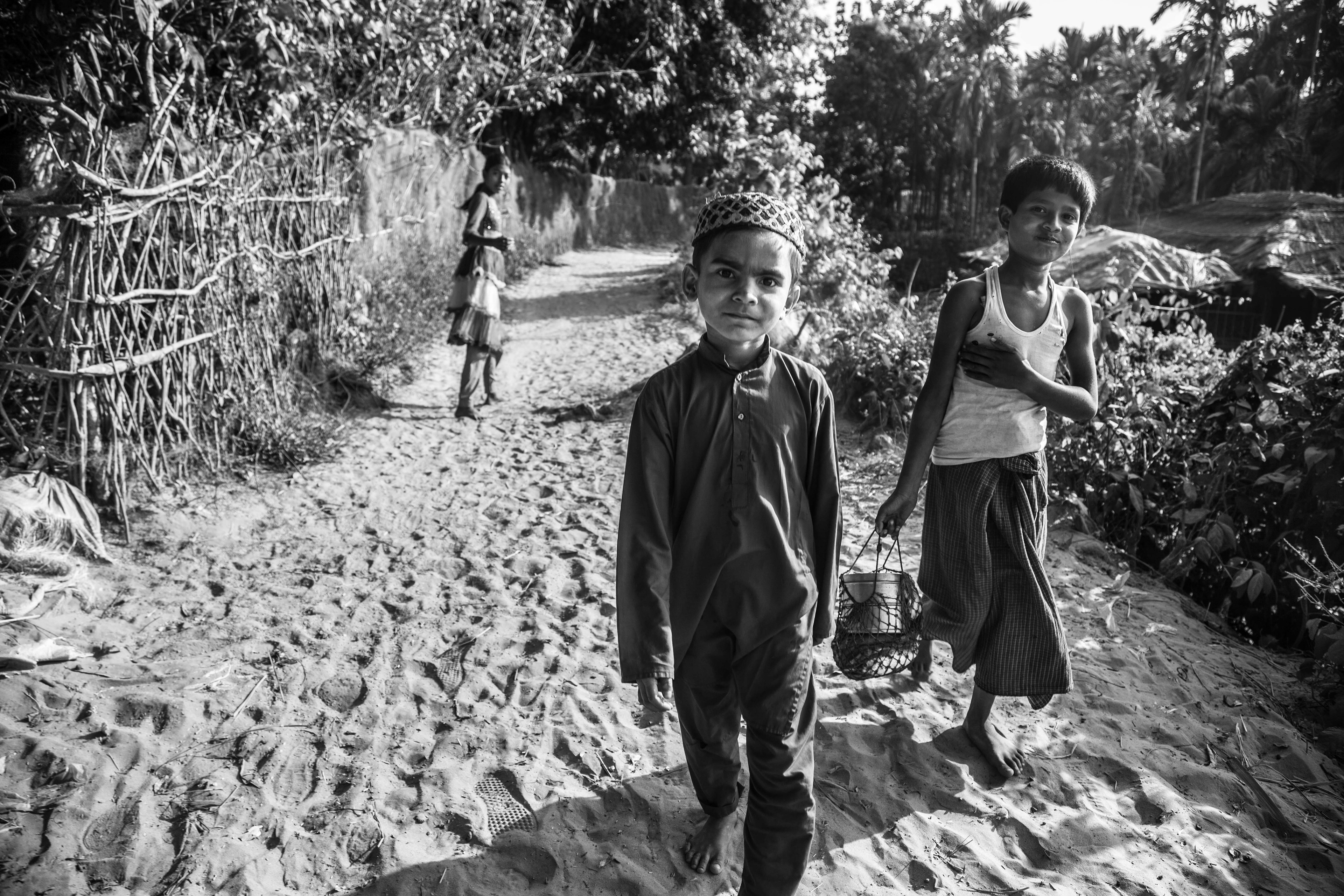 "Resilience and Resourcefulness." Shamlapur, Bangladesh. Jan 2016. A young boy in school clothes comes home from madrasa while another comes back from the beach with some fresh fish. Generous teachers do exist that allow Rohingya children to participate in their schools and lessons, privately or at the local mosque, but some families cannot afford to have their children do anything but work.