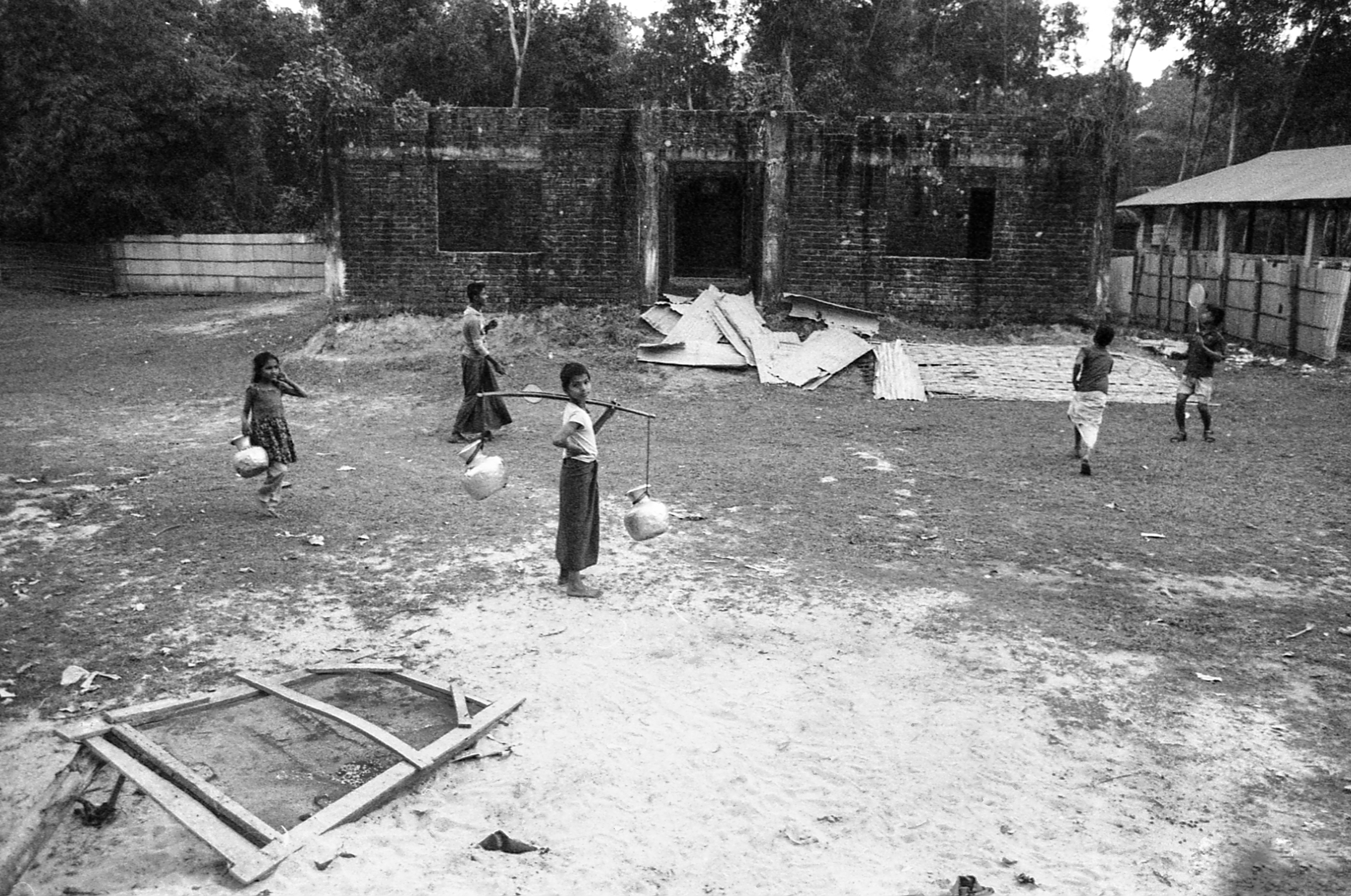 Leda Camp, Teknaf, Bangladesh. Several children bring home jugs of water while others play badminton near the entrance to camp.