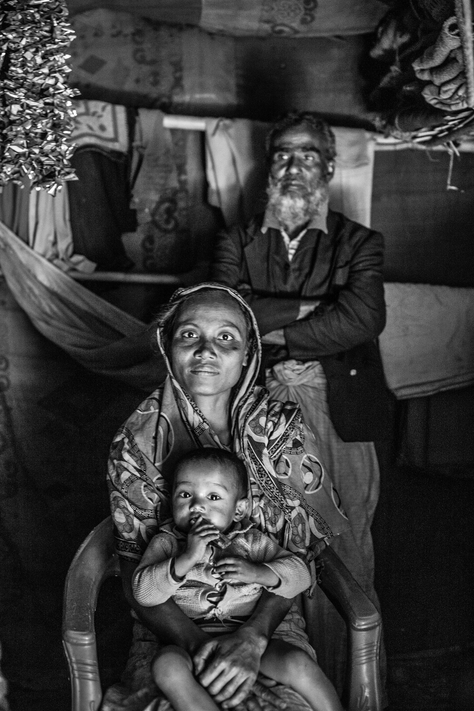 "A Family History." Leda Camp, Teknaf, Bangladesh. Jan 2016. A portrait of Kasim and his wife and daughter. Kasim suffers from memory loss and twitches after his imprisonment where he was tortured by electrocution for allegedly taking part in the Rohingya Solidarity Organization, a militant group that rose up against the Myanmar Armed Forces in the 1990s.