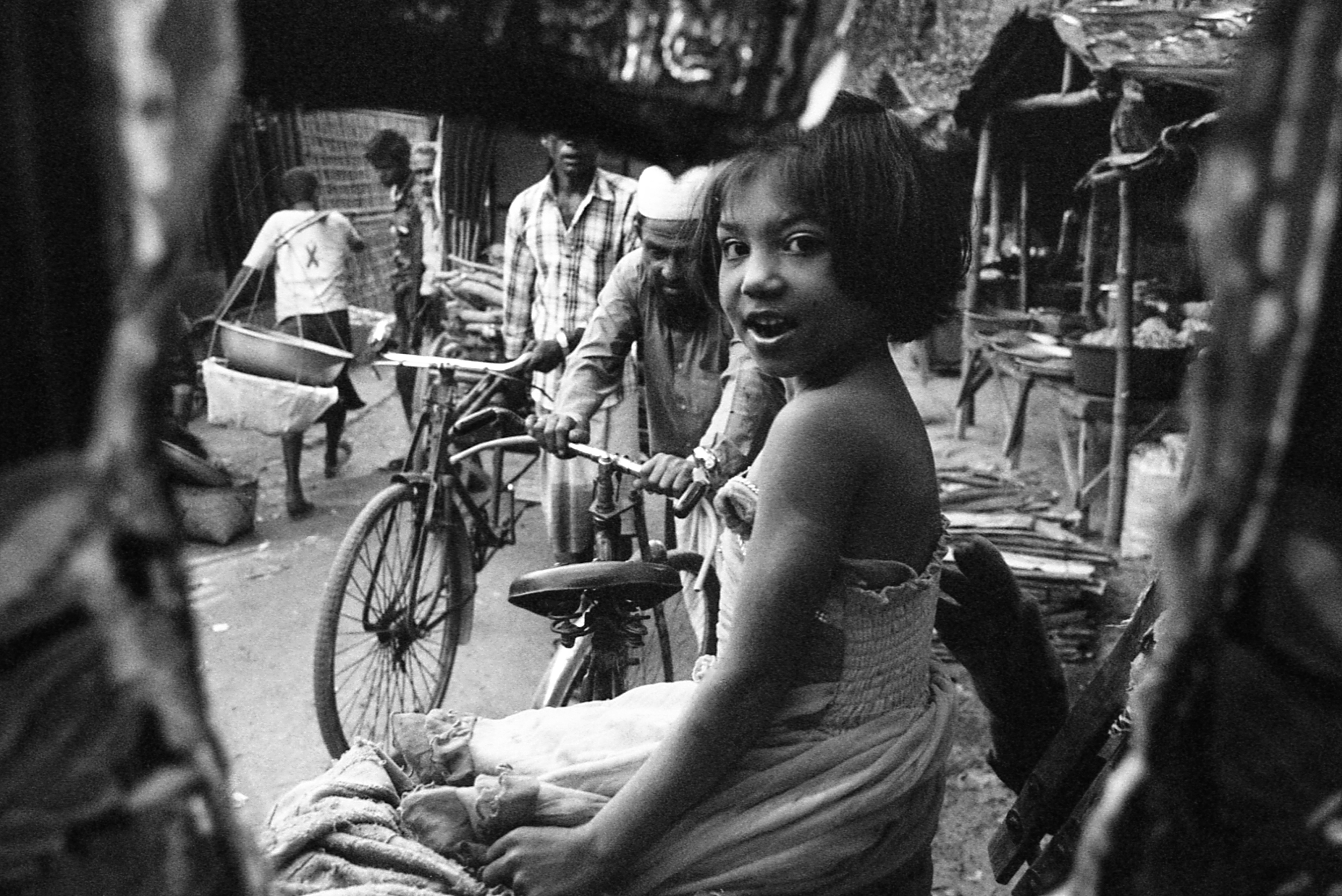 Leda Camp, Teknaf, Bangladesh. A young girl peers through the back of her father's bicycle rickshaw. Many Rohingya risk arrest or worse by seeking employment in the bigger towns like Teknaf or Nhila, a few kilometers each outside of camp.