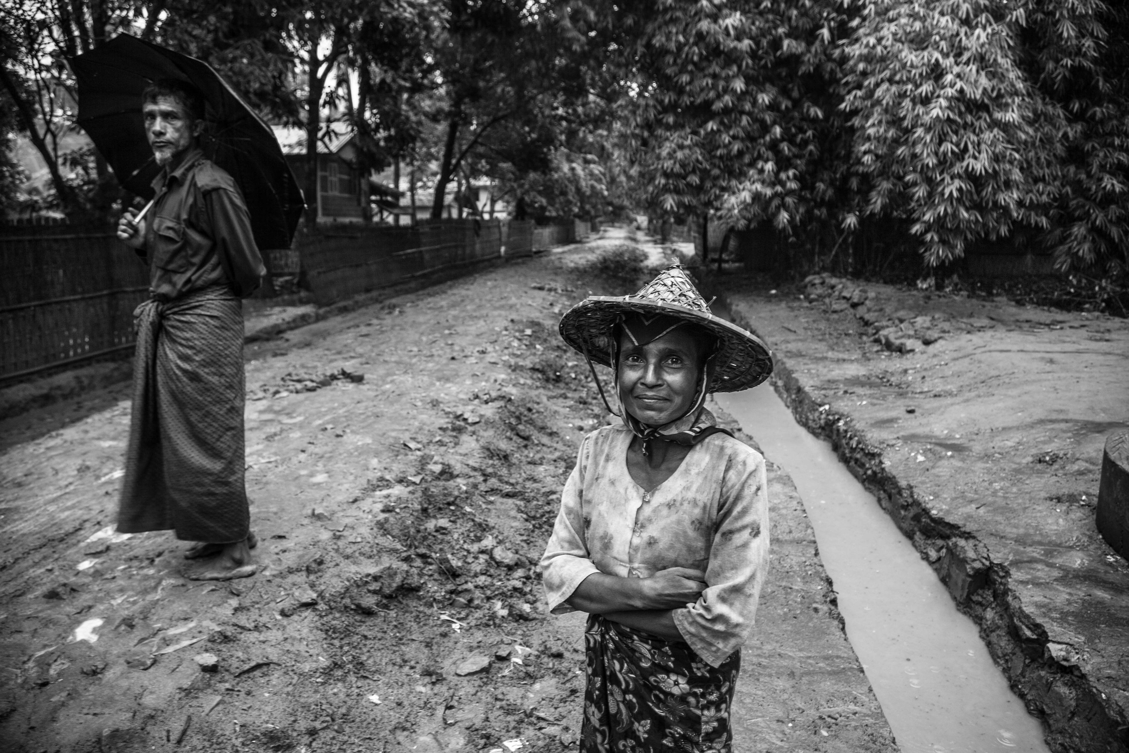 "Isolated." Paungdok, Myanmar. May 2016. As in Sittwe, violence against the Rohingya in Mrauk-U was widespread. Many Rohingya were forcibly displaced and ended up in IDP camps or villages like Paungdok, far from the center of Mrauk-U. They are isolated and without access to schools, hospitals or sufficient food and clean water. Here, a woman and her husband walk barefoot in the rain near the entrance to this largely Muslim village.
