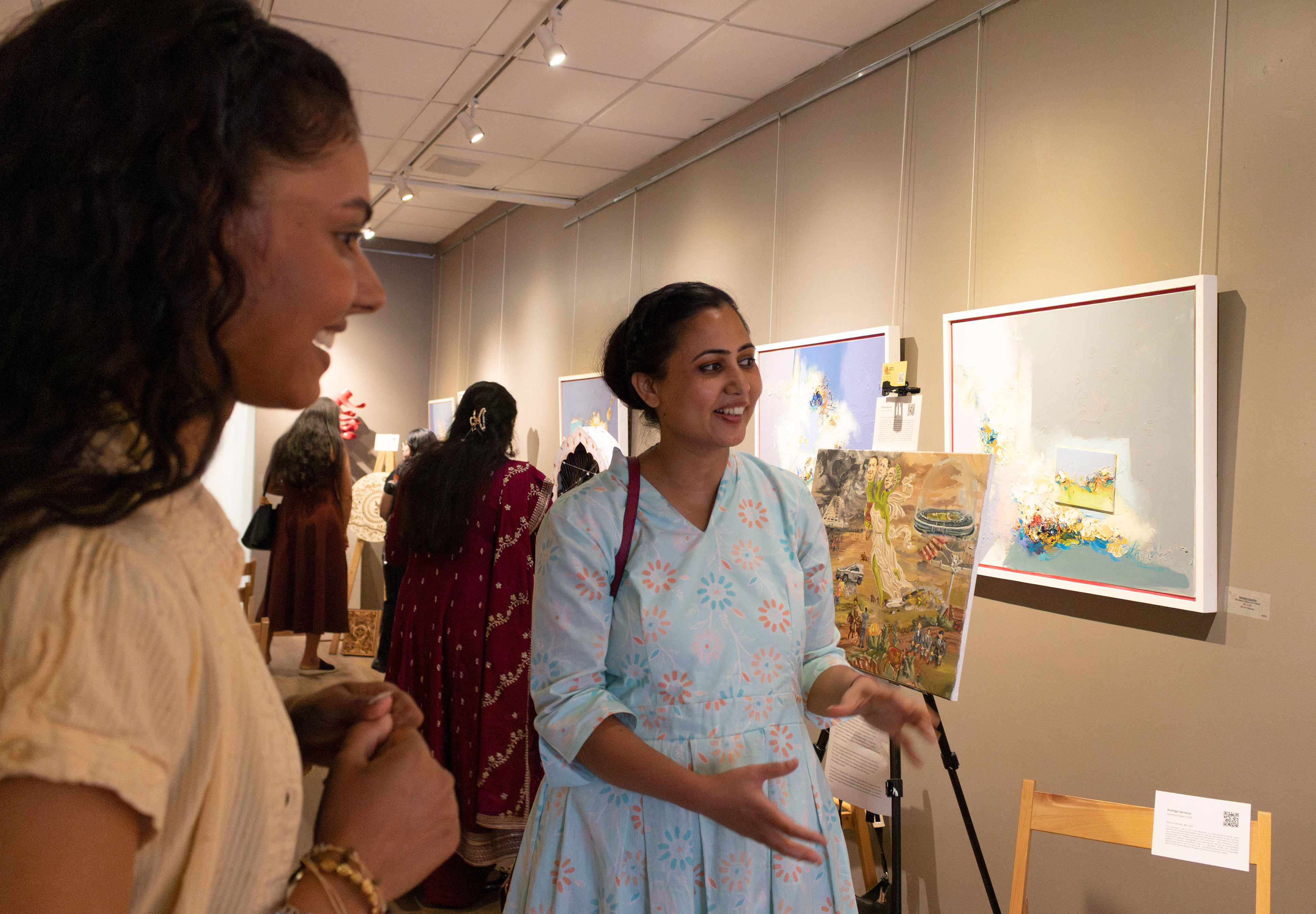 NEW BRUNSWICK, NJ 06/20/2026 CANVAS AND KAHANI: Resin artist Pranali Bharambe and Artist and Rutgers alumna Rushiga Sarveiya discuss her oil painting named “Sudama Nagar.” Central Desi, a South Asian news publication, hosts its first-ever art showcase and open mic at Alfa Art Gallery on Church Street. Photo by Sunah Choudhry.