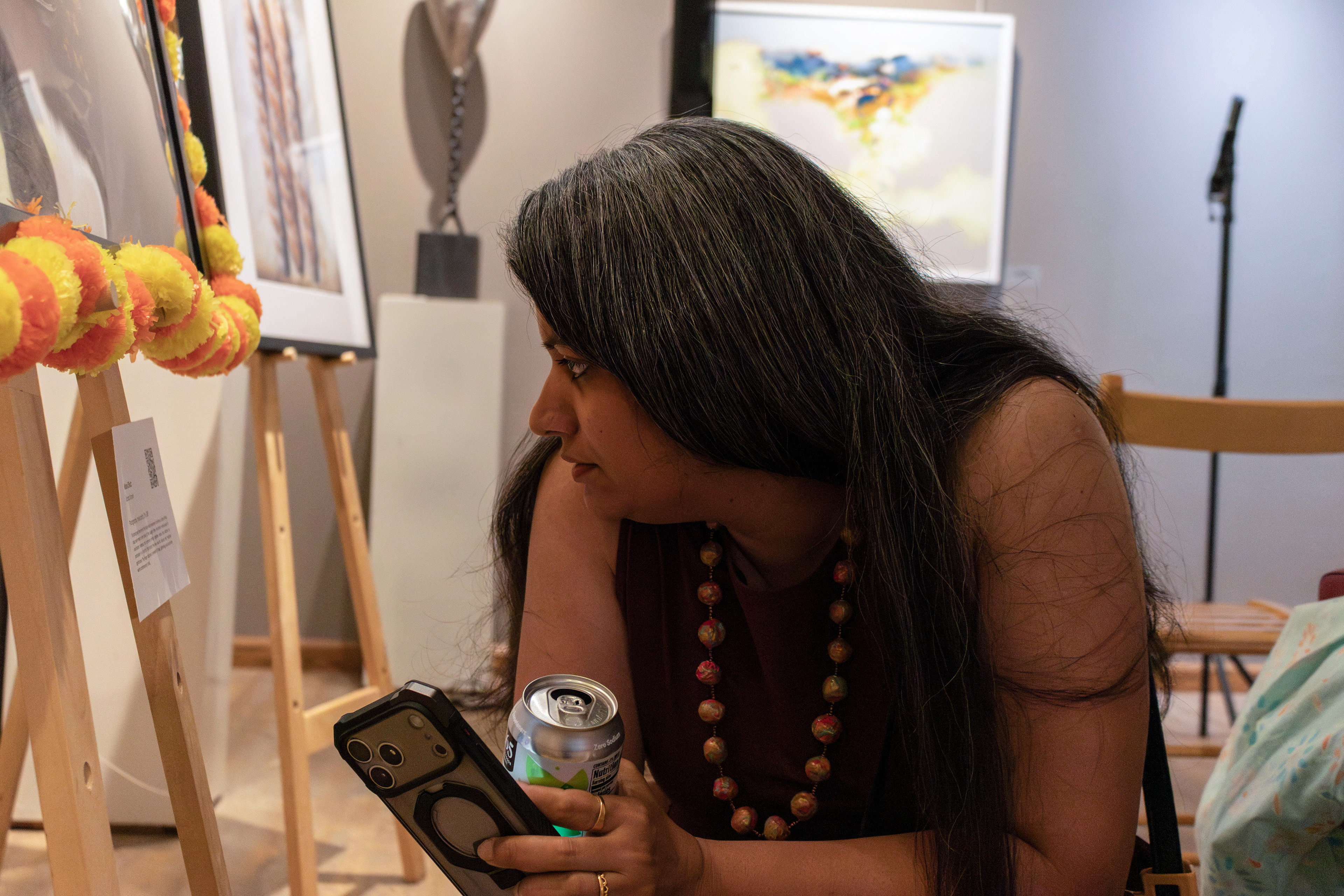 NEW BRUNSWICK, NJ 06/20/2026 CANVAS AND KAHANI: Pyrographist Janhavi Firke reads Mansi Bhatt’s description card for her film photography work. Central Desi, a South Asian news publication, hosts its first-ever art showcase and open-mic at Alfa Art Gallery on Church Street. Photo by Sunah Choudhry.