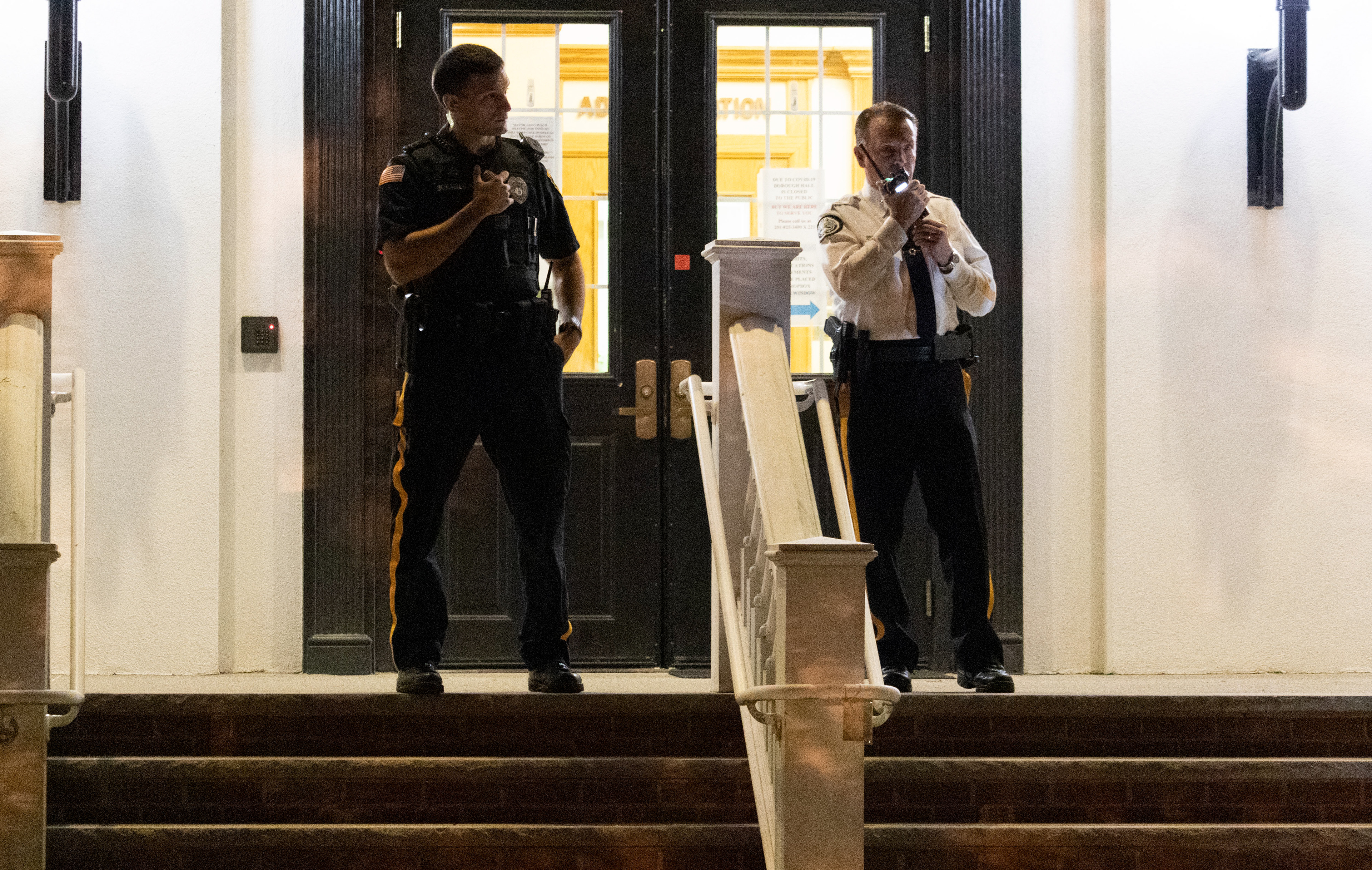 Chief of Police Bryan Gurney stands in front of the doors of town hall with an accompanying officer. Gurney calls in a report of a black vehicle circling the street harassing protesters shouting, "White power." Photo by Sunah Choudhry. (Photo/Sunah Choudhry)