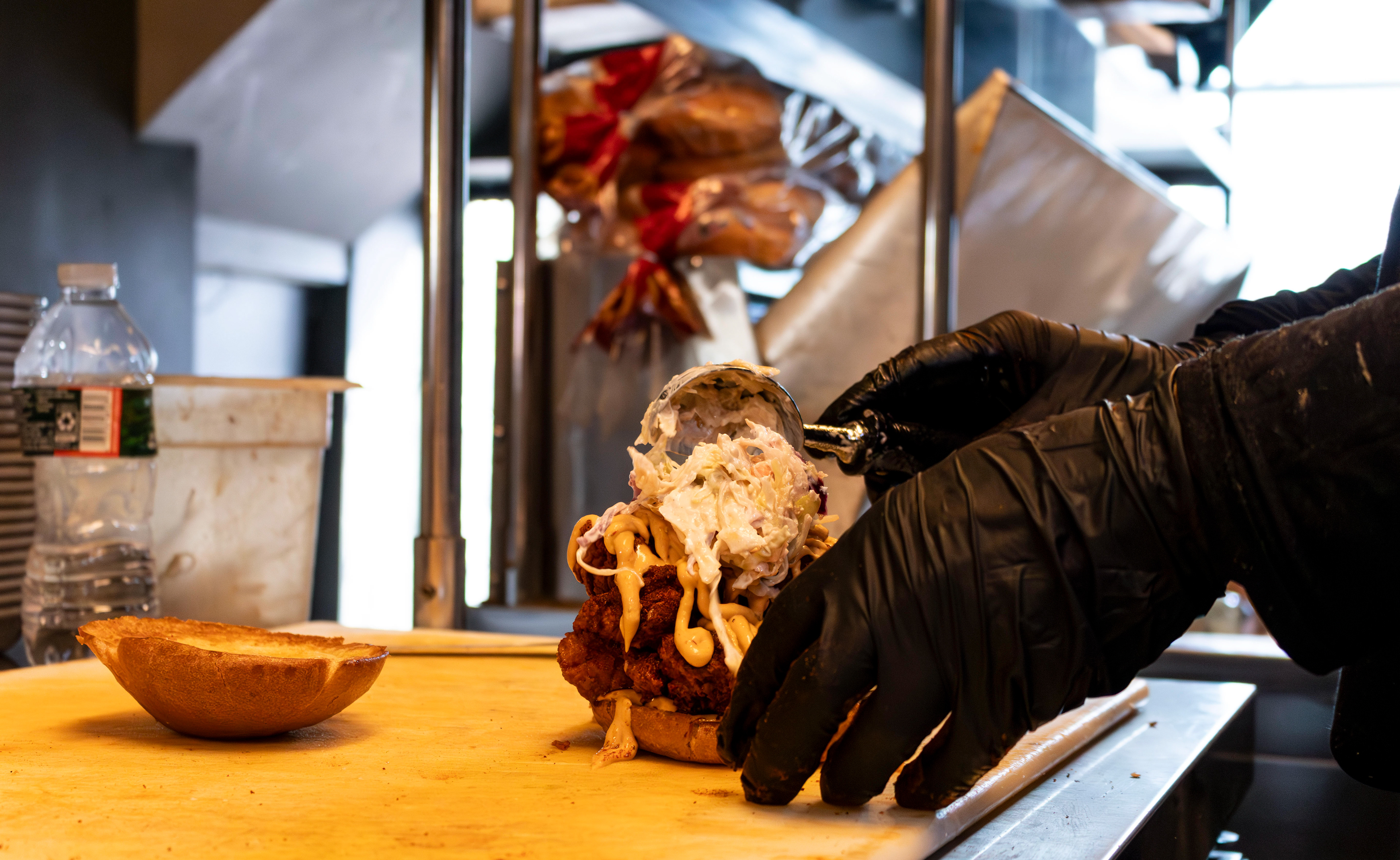 A cook pours a scoop of coleslaw onto a fried chicken sandwich in Food Street's kitchen. Photo by Sunah Choudhry.