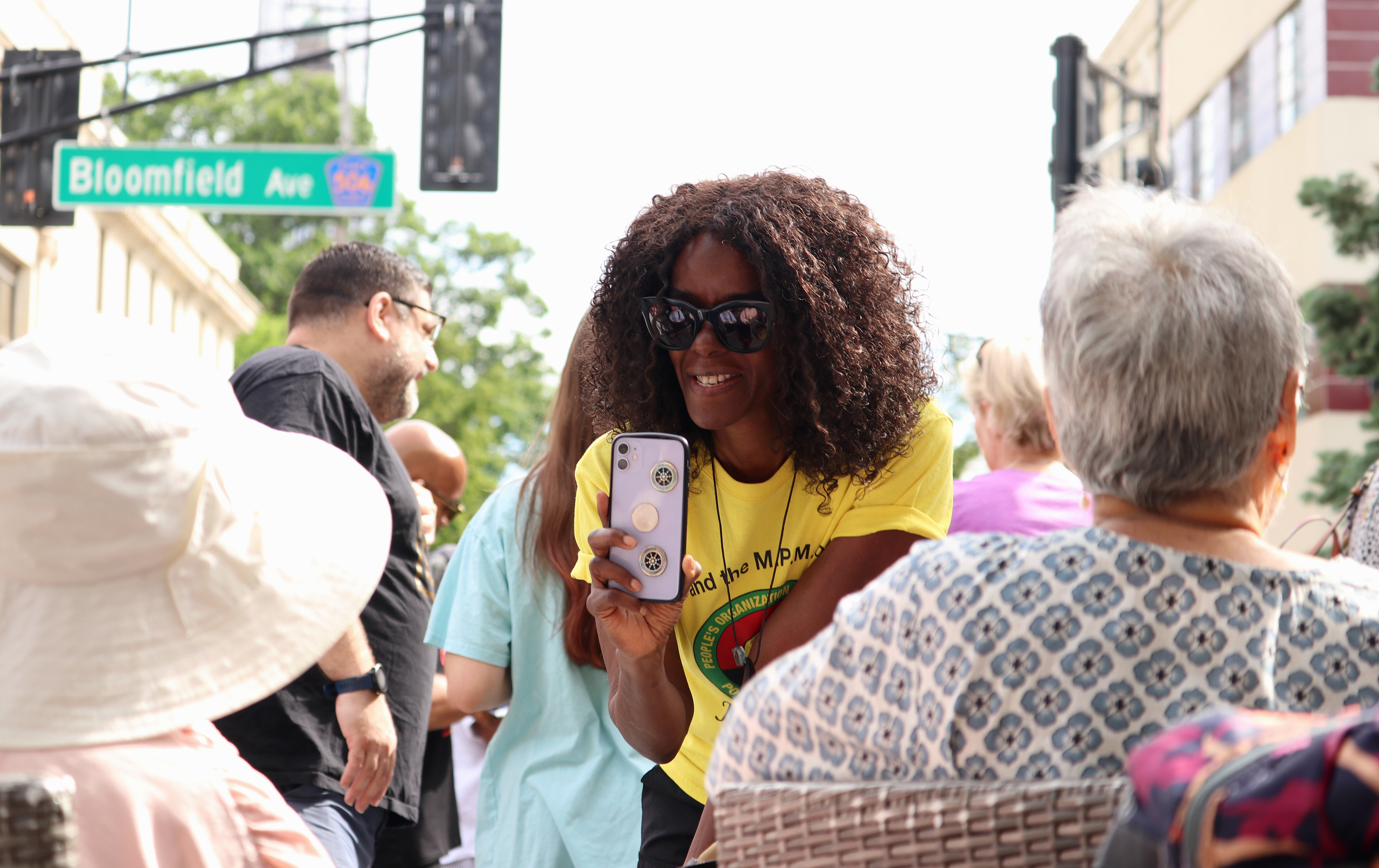 MONTCLAIR, NJ 06/19/2026 JUNETEENTH FLAG RAISING: People’s Organization For Progress’ social media ambassador, Susan Saintweather, records and asks attendees how they are feeling at Montclair’s Juneteenth flag-raising ceremony on the corner of Church Street and Bloomfield Ave. Montclair residents gather to honor and celebrate Juneteenth, listen to local politicians and leaders, and watch a performance by the students from Beyond the Boogie Dance Company. Photo by Sunah Choudhry.