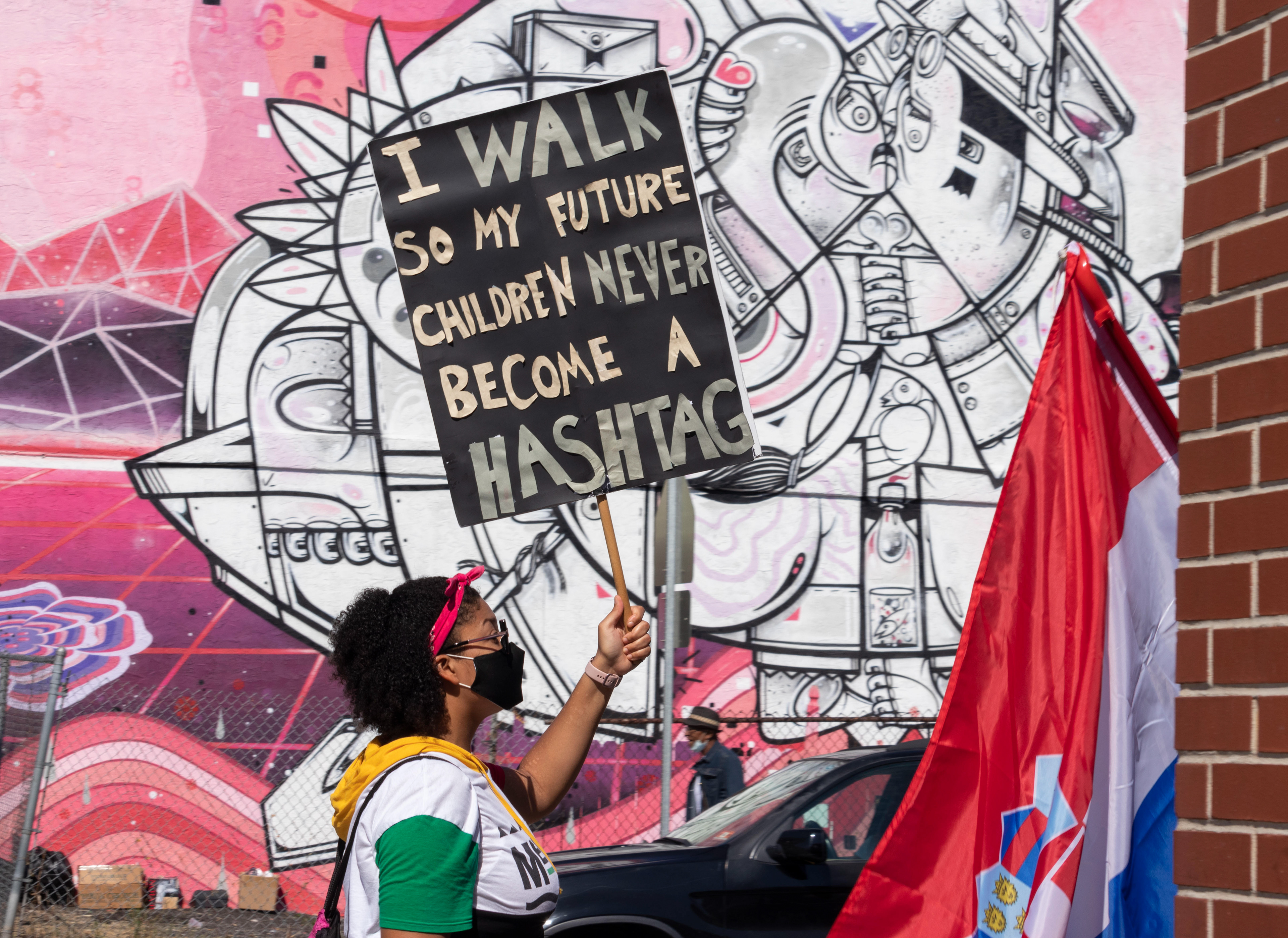 A woman holds up a sign that reads, “I walk so my future children never become a hashtag.”
