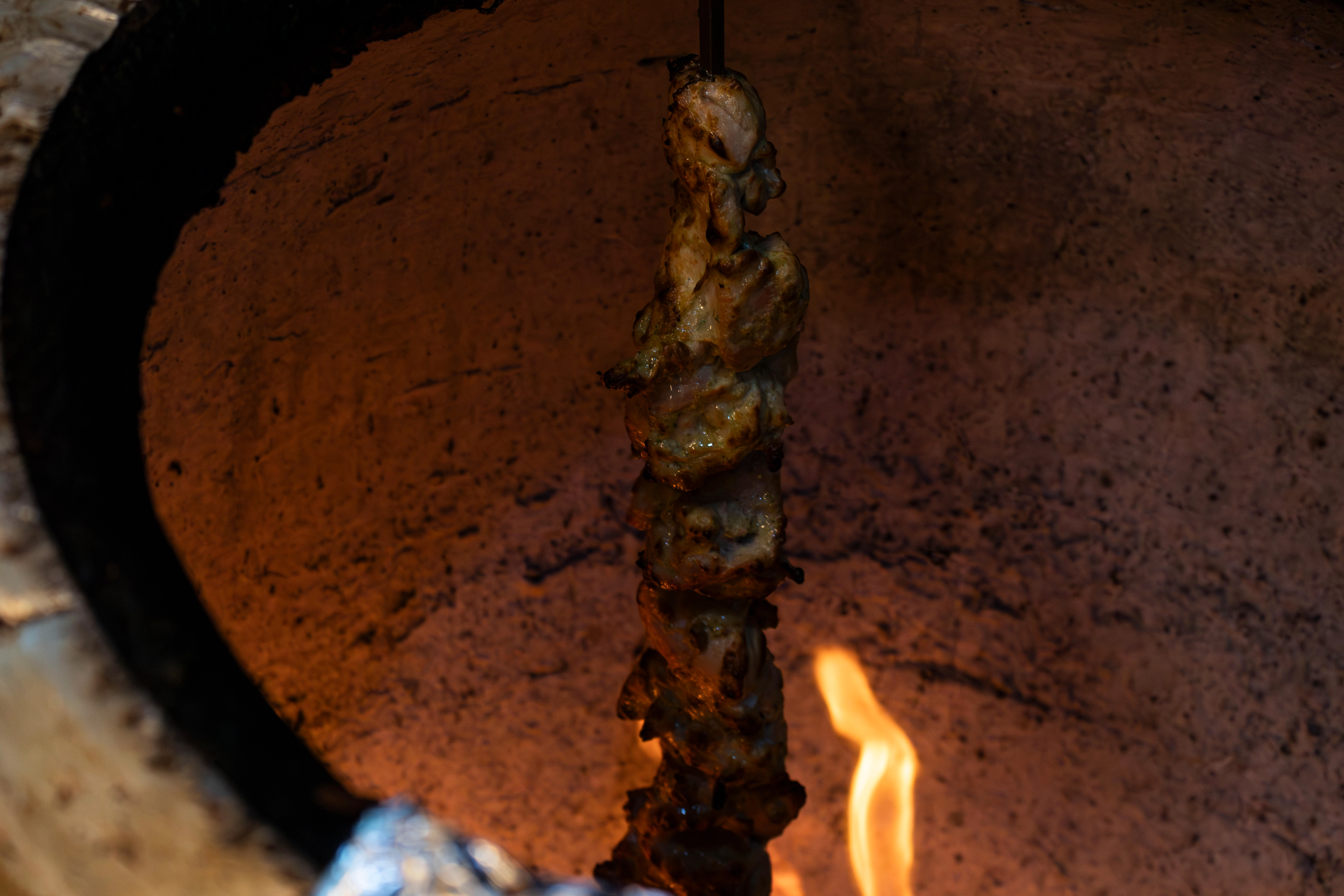 A skewer of chicken tikka cubes standing up straight in a cylinder tandoor. Photo by Sunah Choudhry.